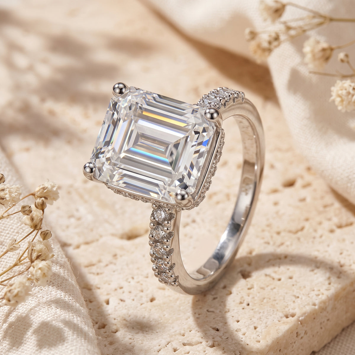 Close-up of a silver ring with a large clear emerald-cut stone, four-prong setting, and pavé shank.