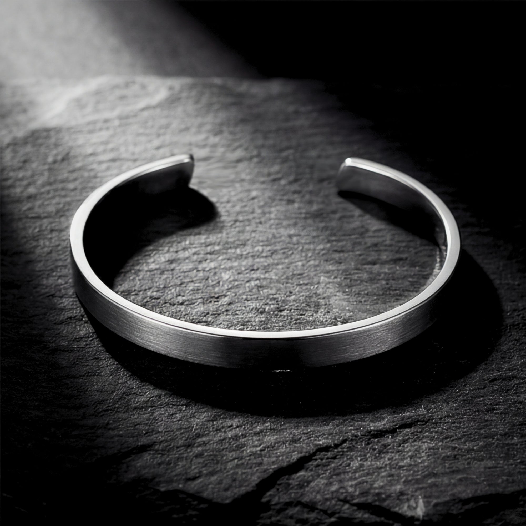Brushed silver stainless steel cuff bracelet resting on a dark textured stone surface.