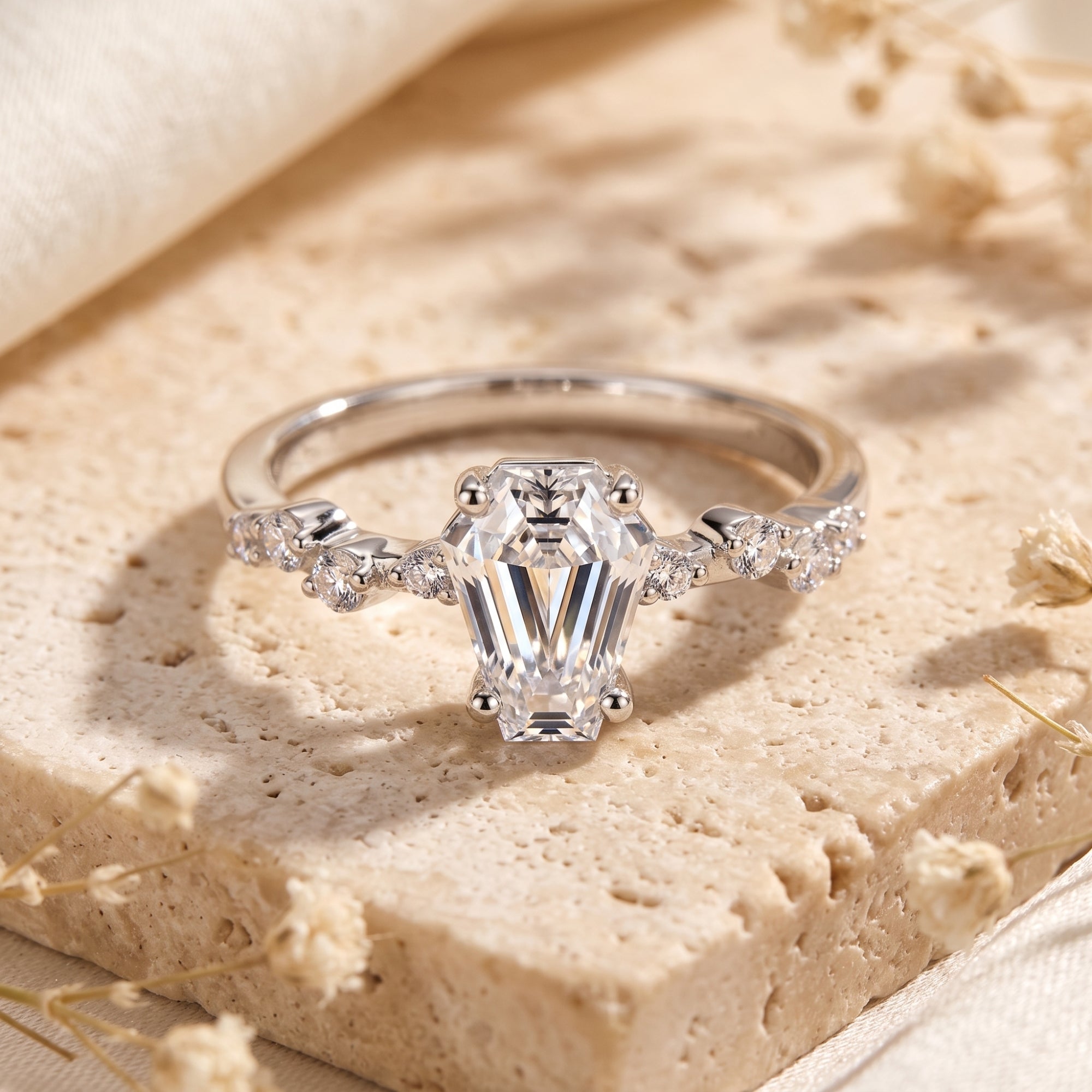 Silver Rosmerta ring with a coffin-cut simulated diamond on a textured stone surface with dried flowers.