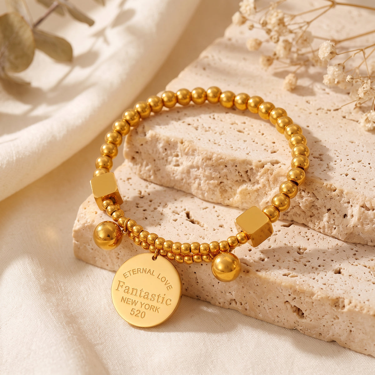 Gold-tone double-strand beaded bracelet with a stamped disc charm resting on layered stone.
