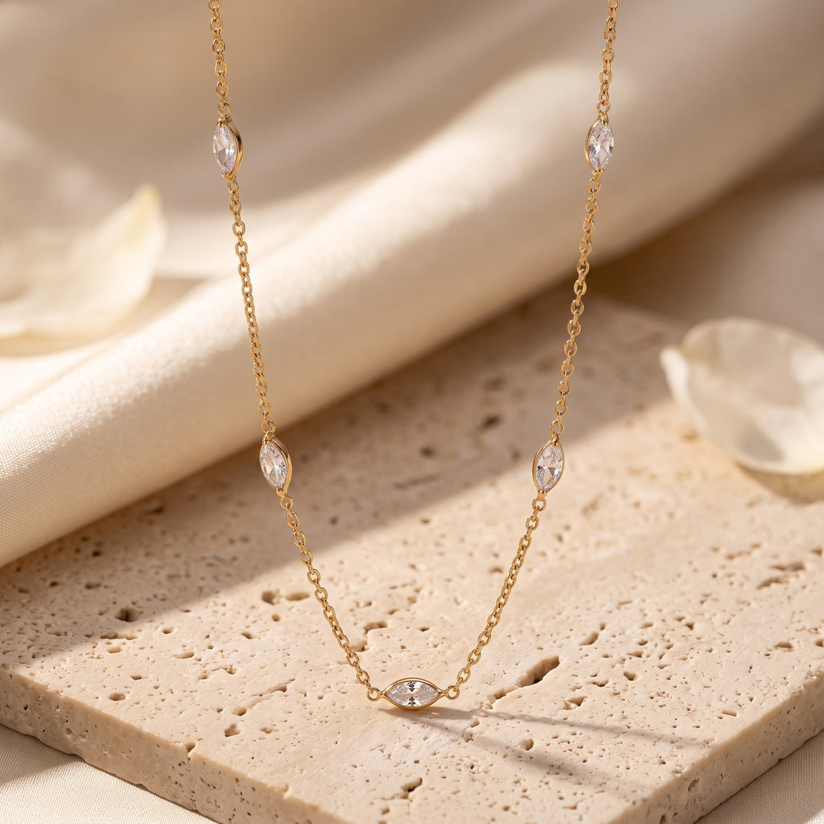 Gold-tone station necklace with clear marquise stones draped over a porous beige stone slab.