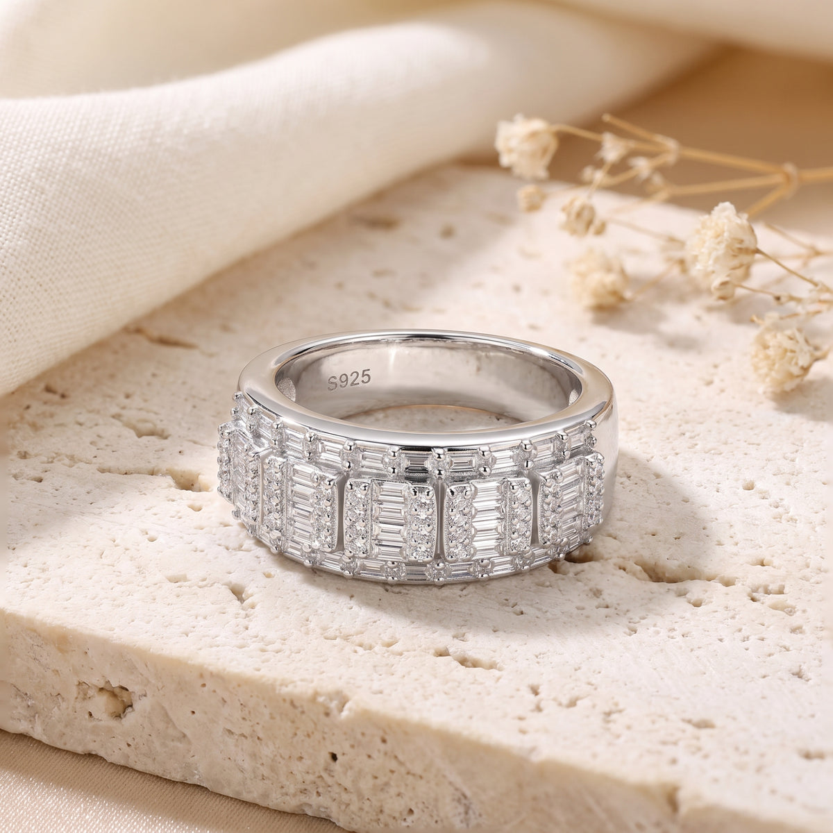 Silver mosaic band ring with baguette and round clear stones resting on a textured stone block.
