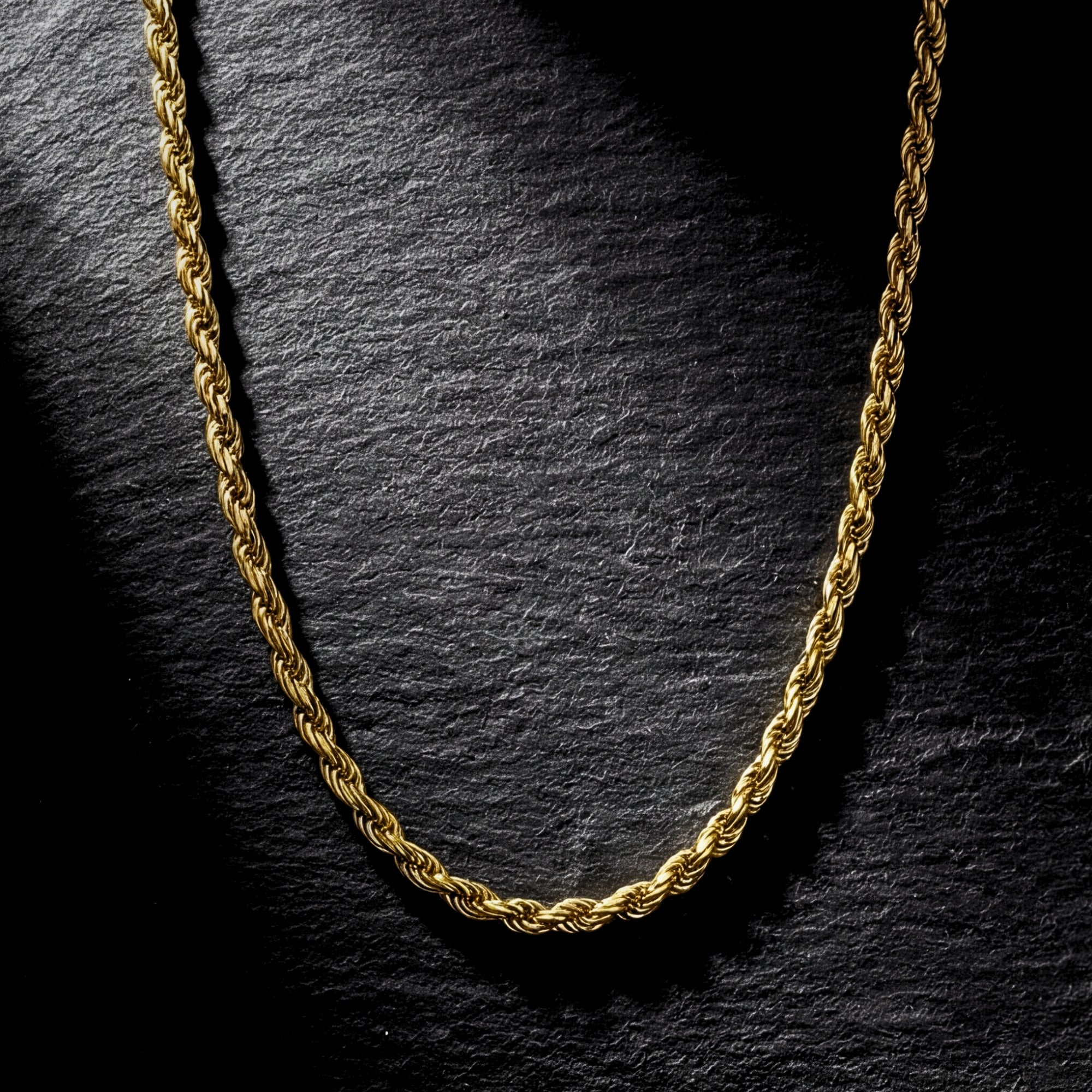 Gold stainless steel 2.5mm rope chain draped on a dark textured stone surface.