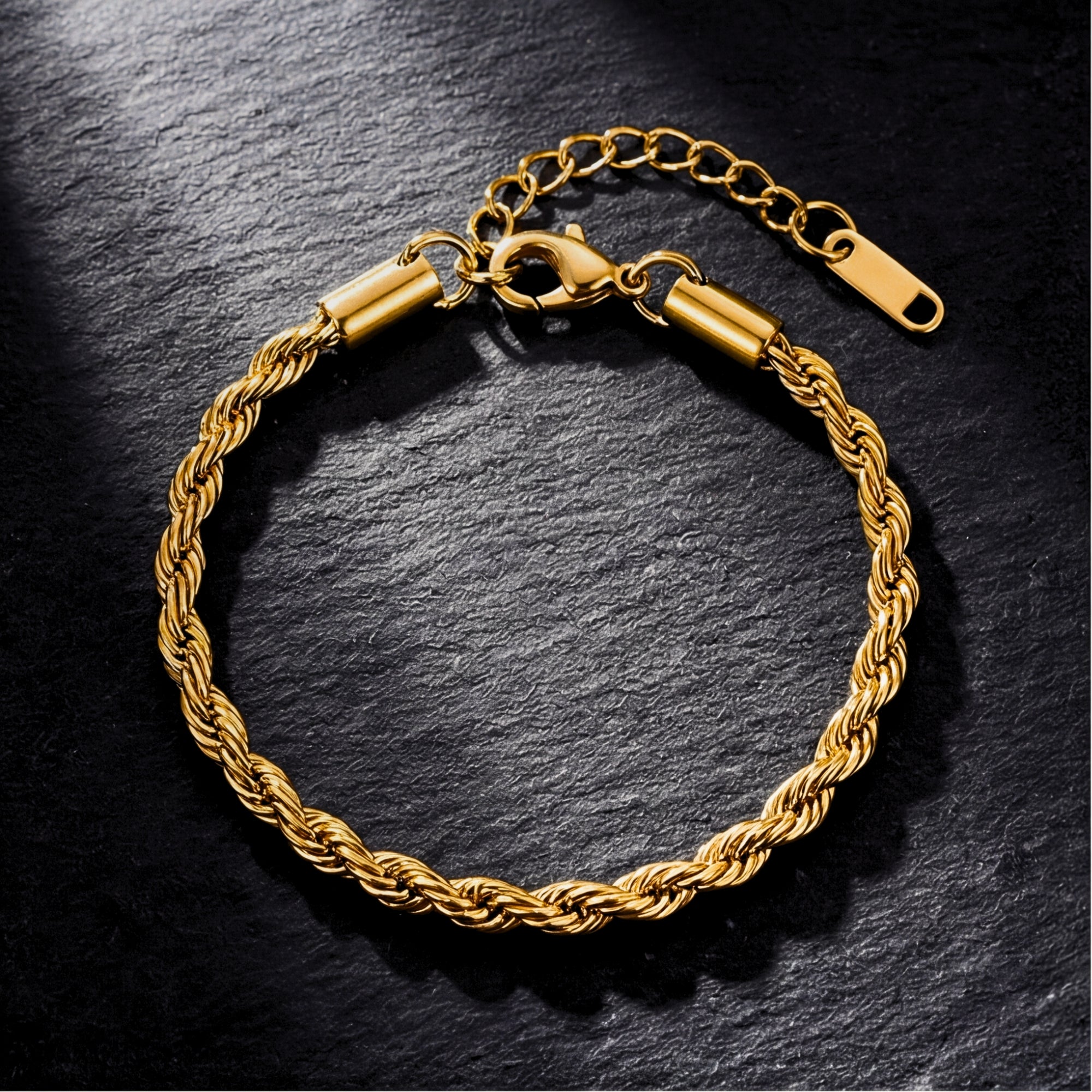 Gold stainless steel rope bracelet with lobster clasp and extender chain on a dark stone background.