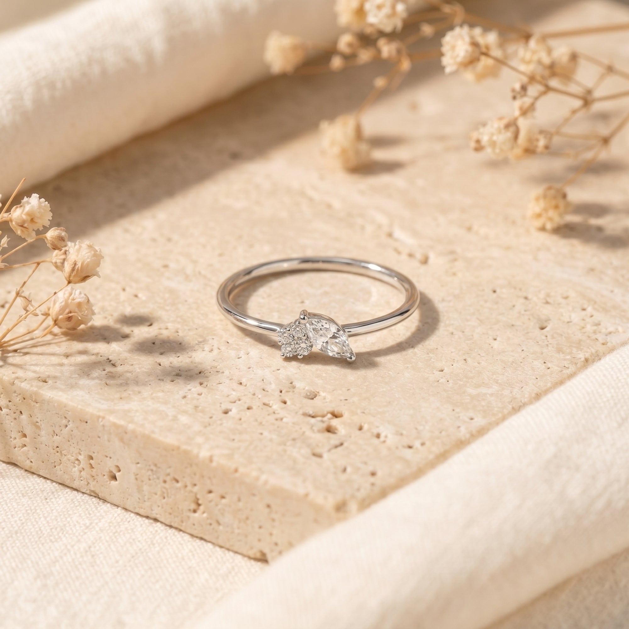 Silver marquise moissanite cluster ring on stone with dried flowers.