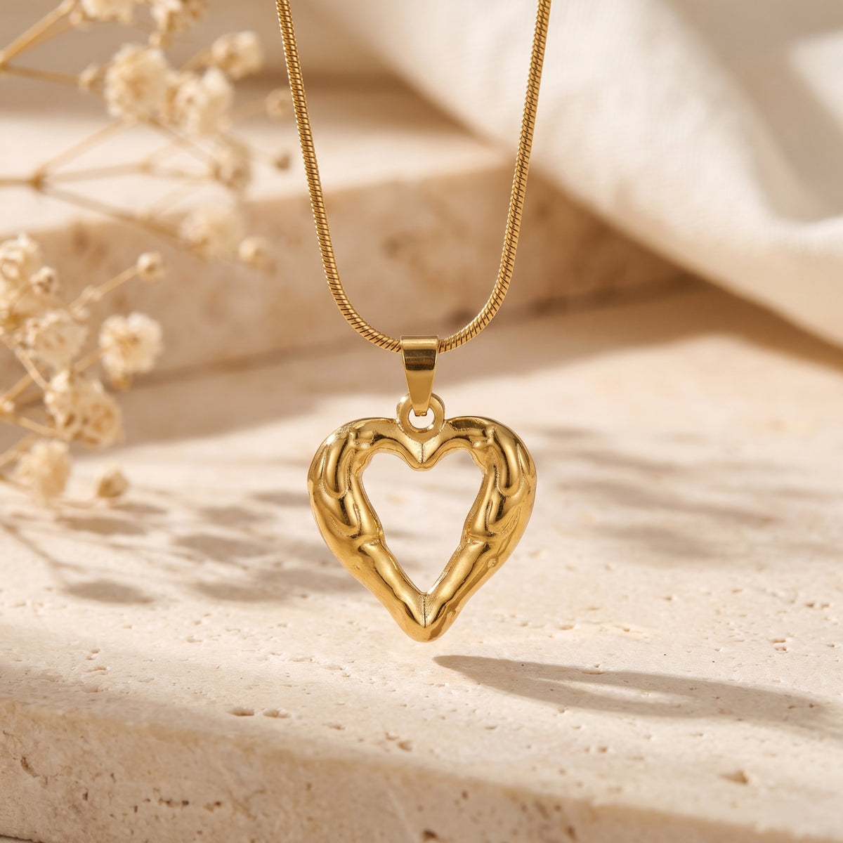 Gold-tone molten open heart pendant hanging from a snake chain over a stone background.