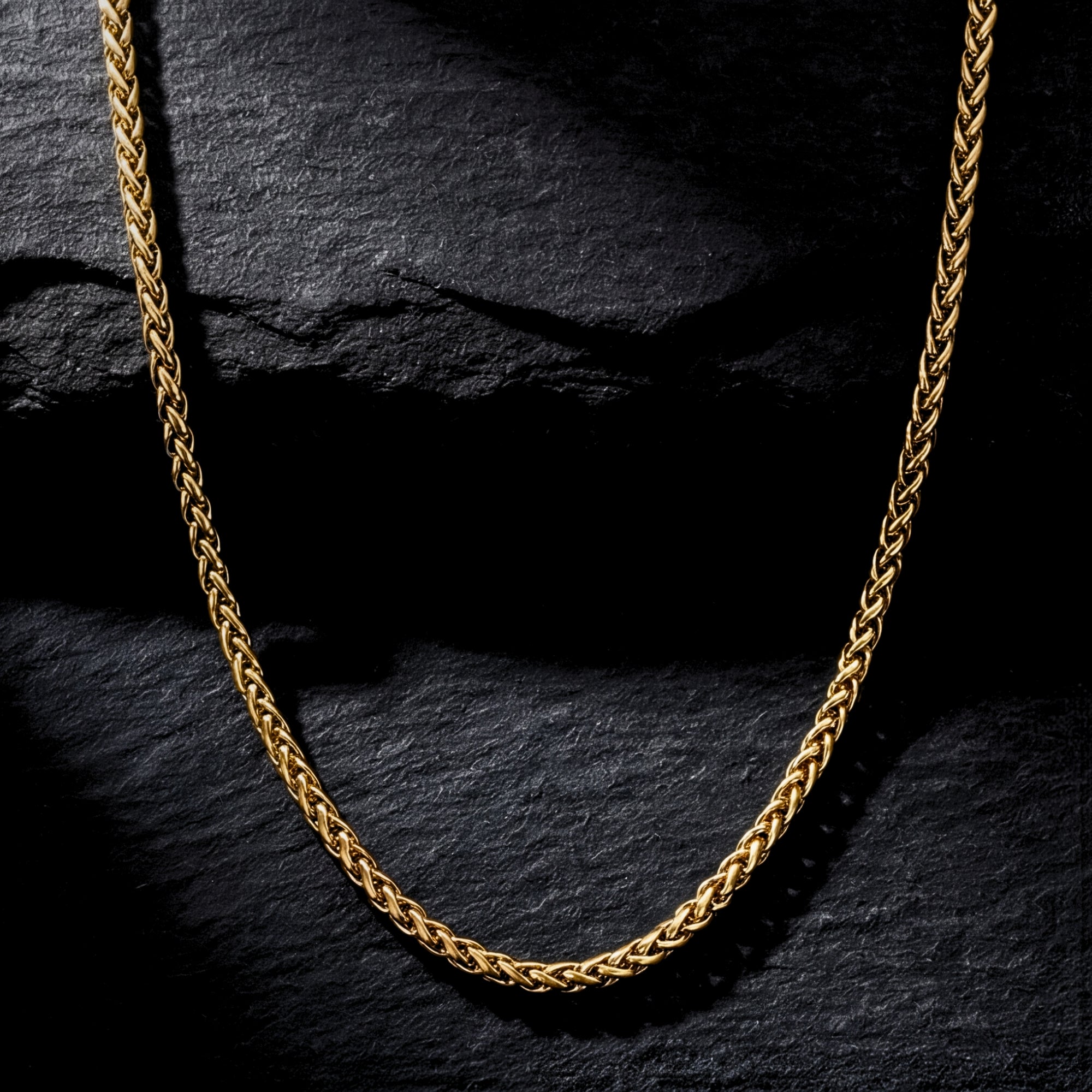 Gold stainless steel wheat chain necklace displayed on a dark textured stone background.