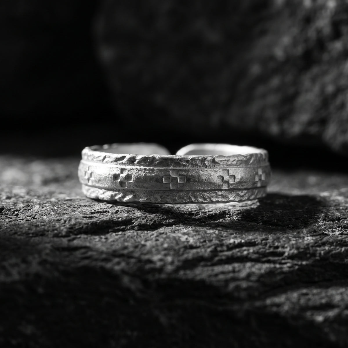 Macro view of the etched silver open band ring with geometric cross-like motifs, resting on dark rock.
