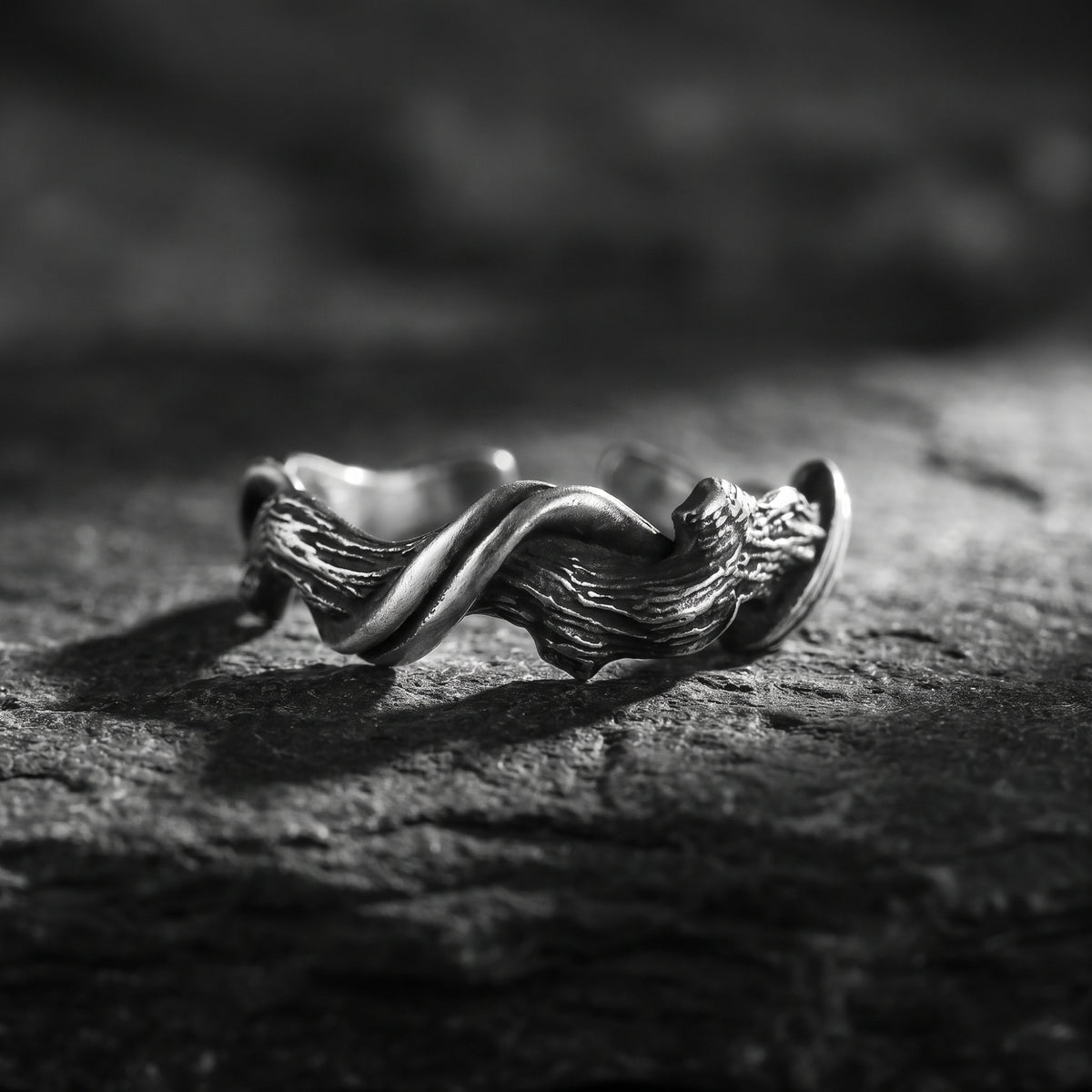 Front close-up of a silver open band ring with a wood-grain twist texture resting on rough stone.