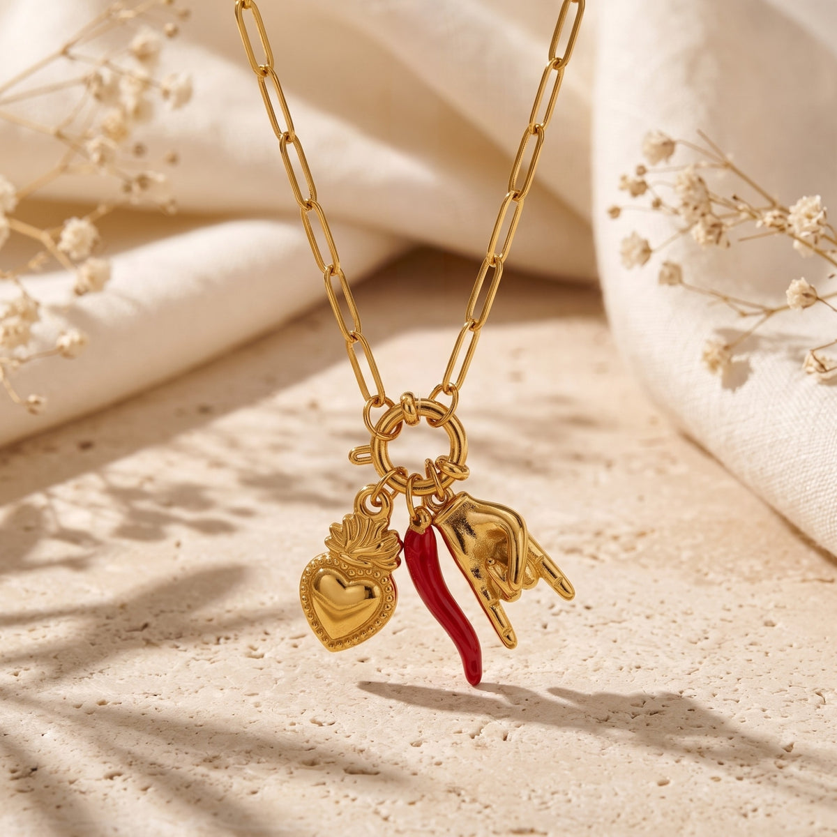 Close-up of a gold-tone paperclip necklace with heart, red pepper, and horned-hand charms.