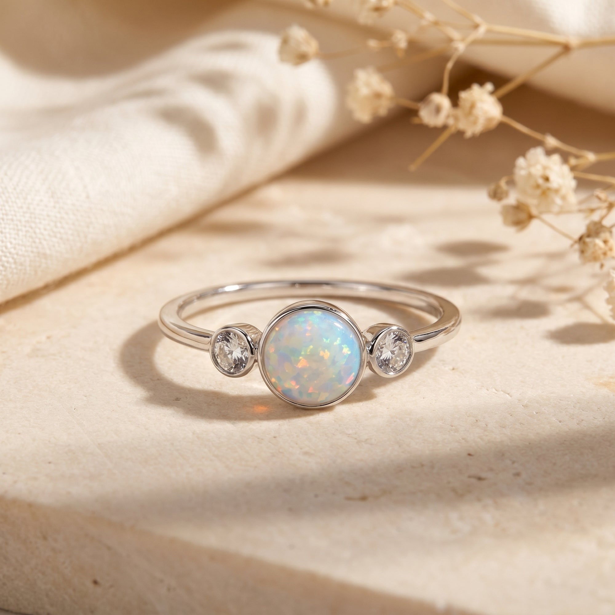 Sterling silver three-stone ring with round white opal cabochon and zircons on a stone surface.