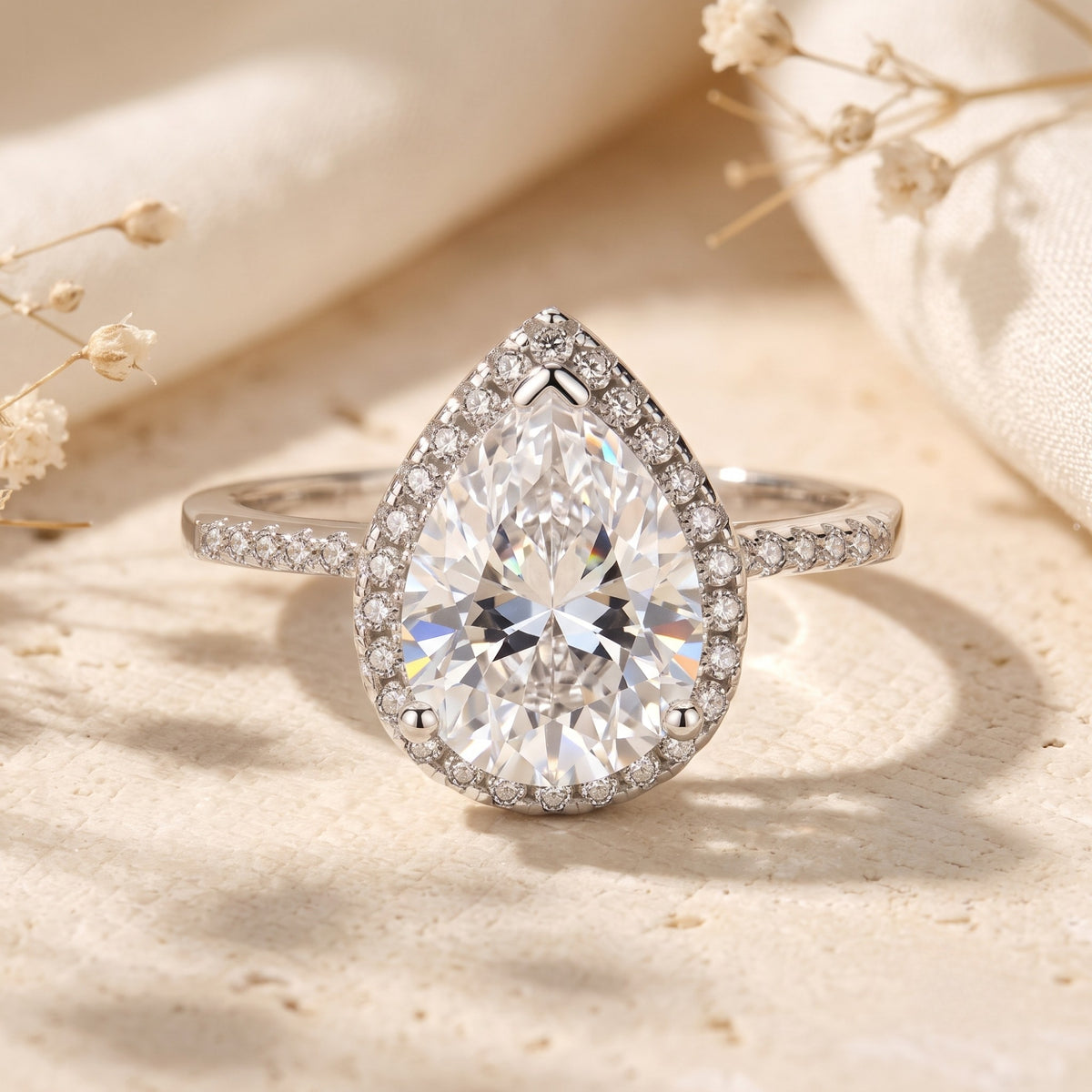 Front view of a silver ring with a large pear-cut center stone surrounded by a halo of round pavé accents.