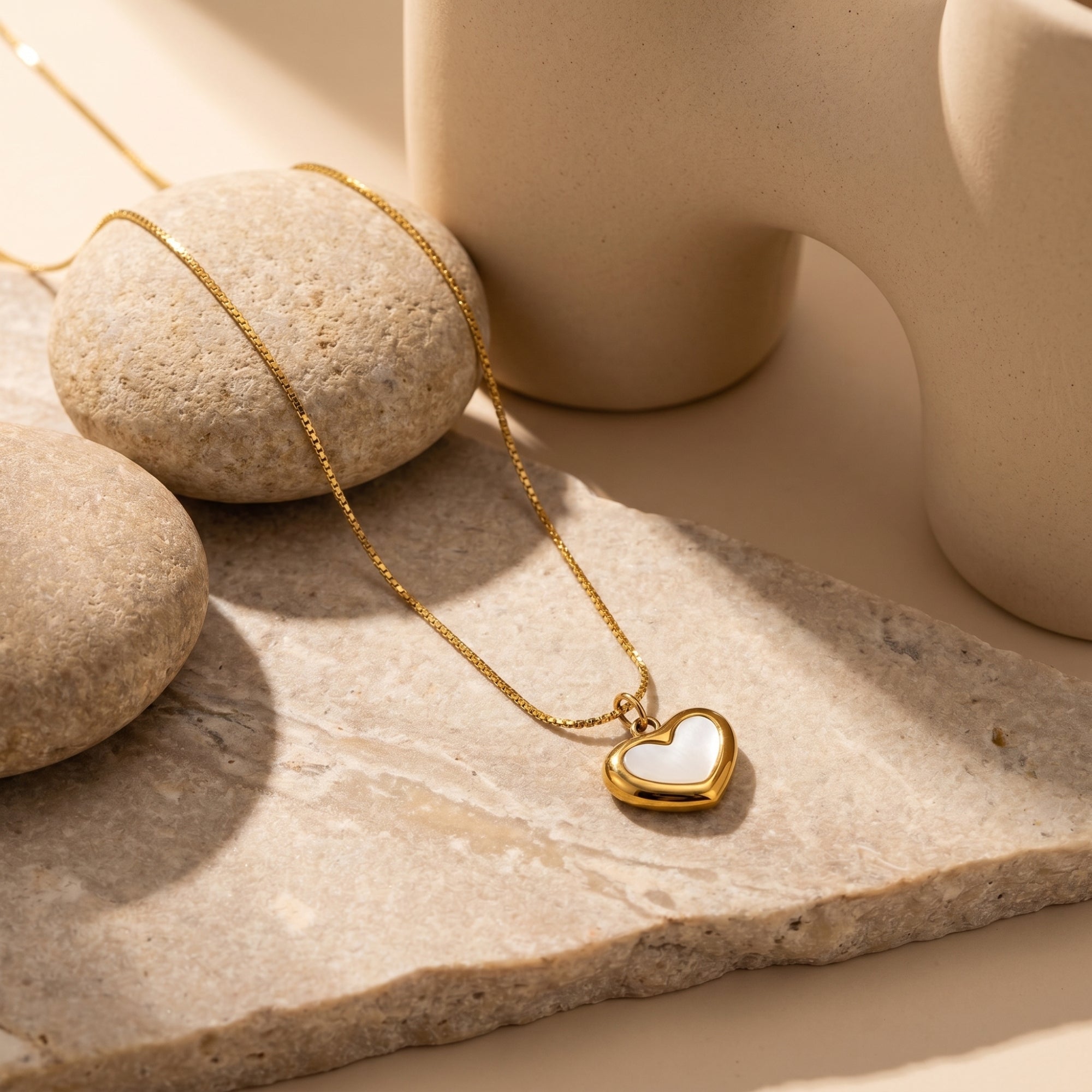 Gold heart necklace with white inlay on a stone slab in a styled lifestyle setting.