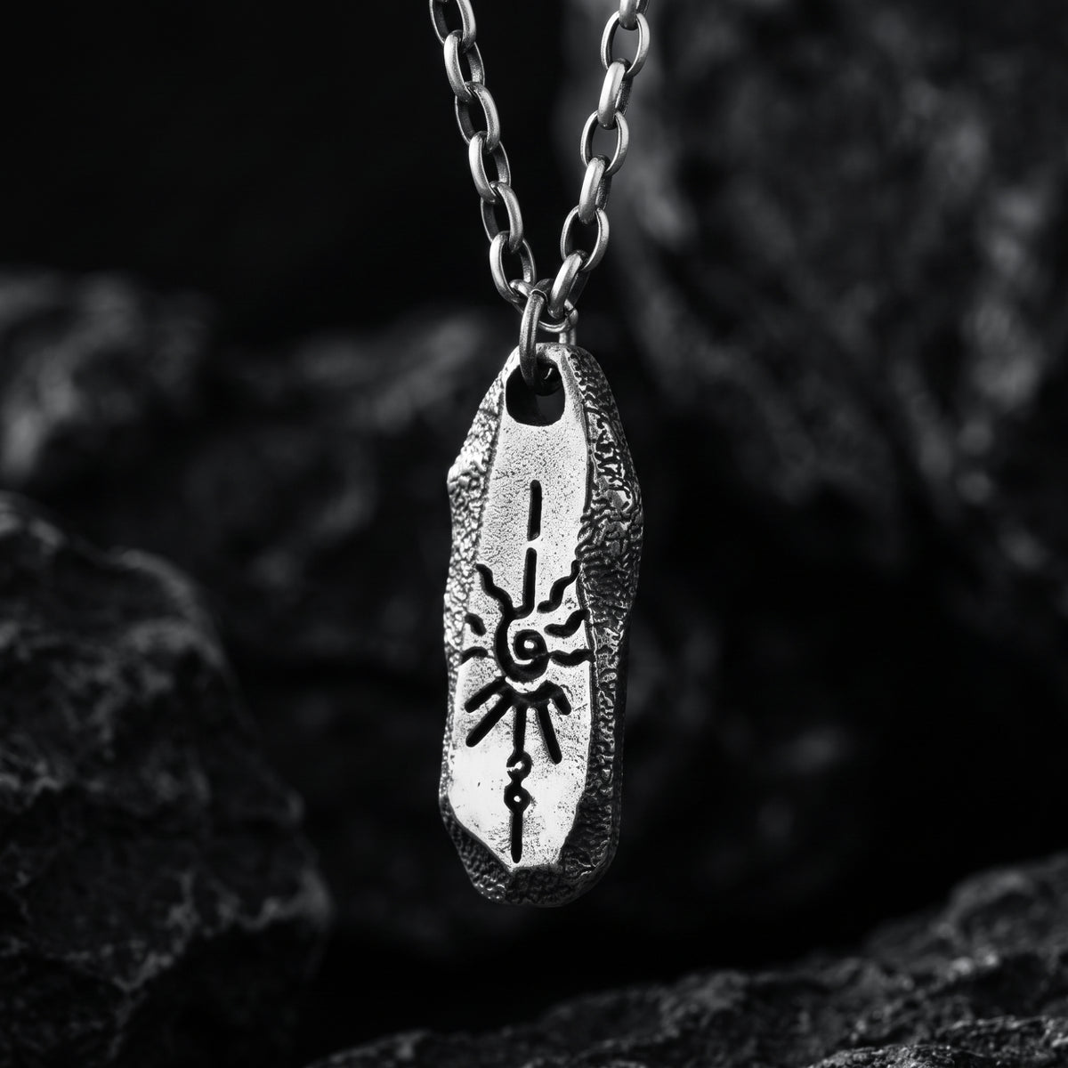 Close-up of a silver bar pendant with an embossed solar motif and textured edges hanging from a chain.