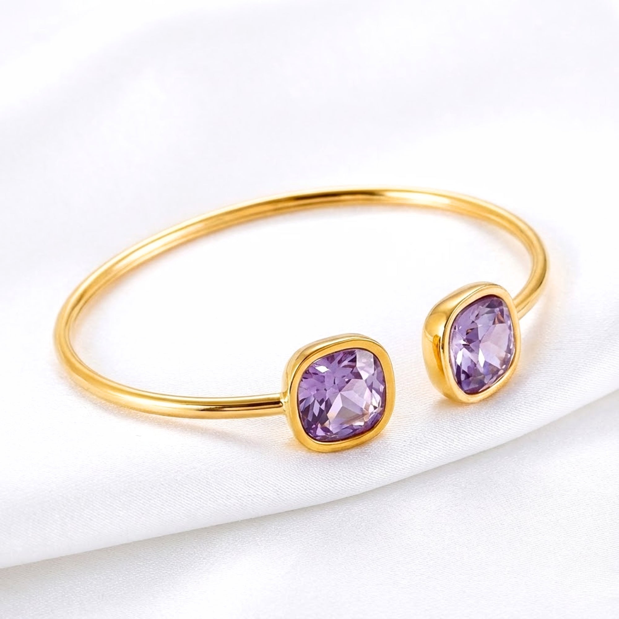 Gold-coated stainless steel Aurelia bangle with cushion-cut simulated amethyst stones on white fabric.
