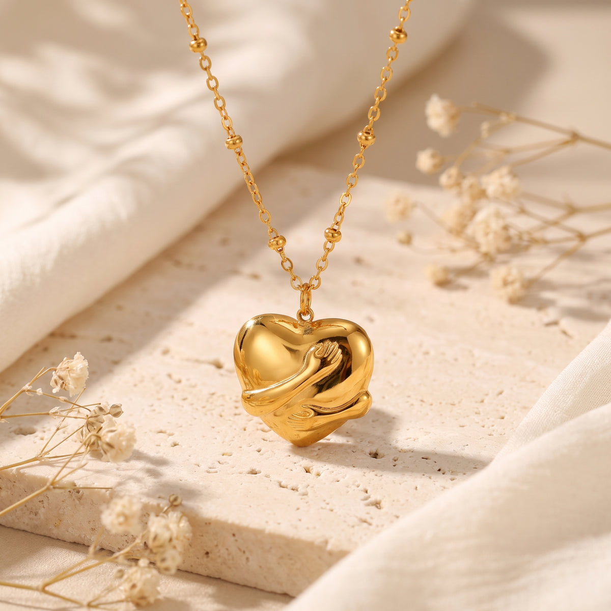 Close-up of a gold-toned heart pendant wrapped in sculpted hands, hanging on a beaded station chain.