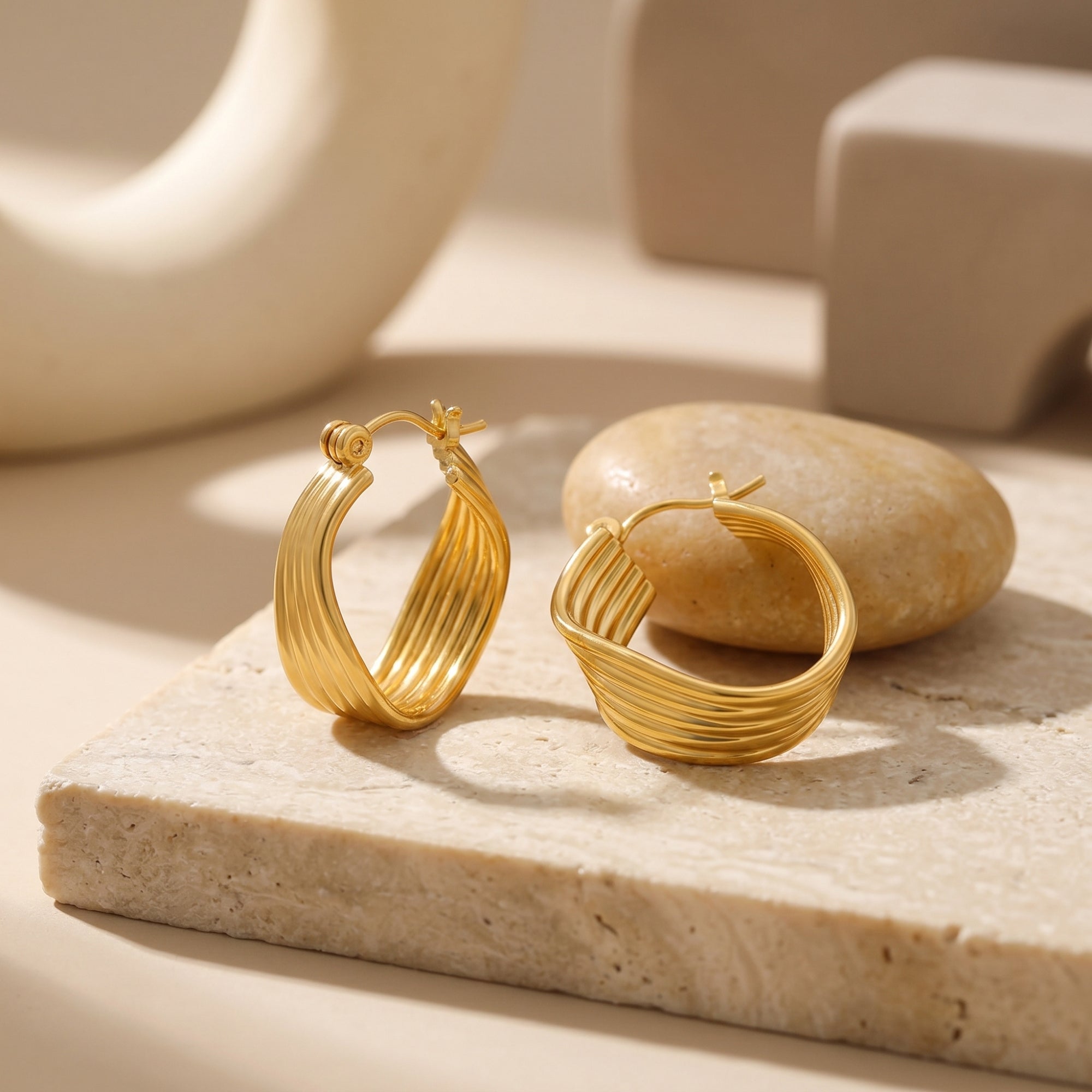 Isolina multi-row hoop earrings in 18K gold PVD on a stone slab.