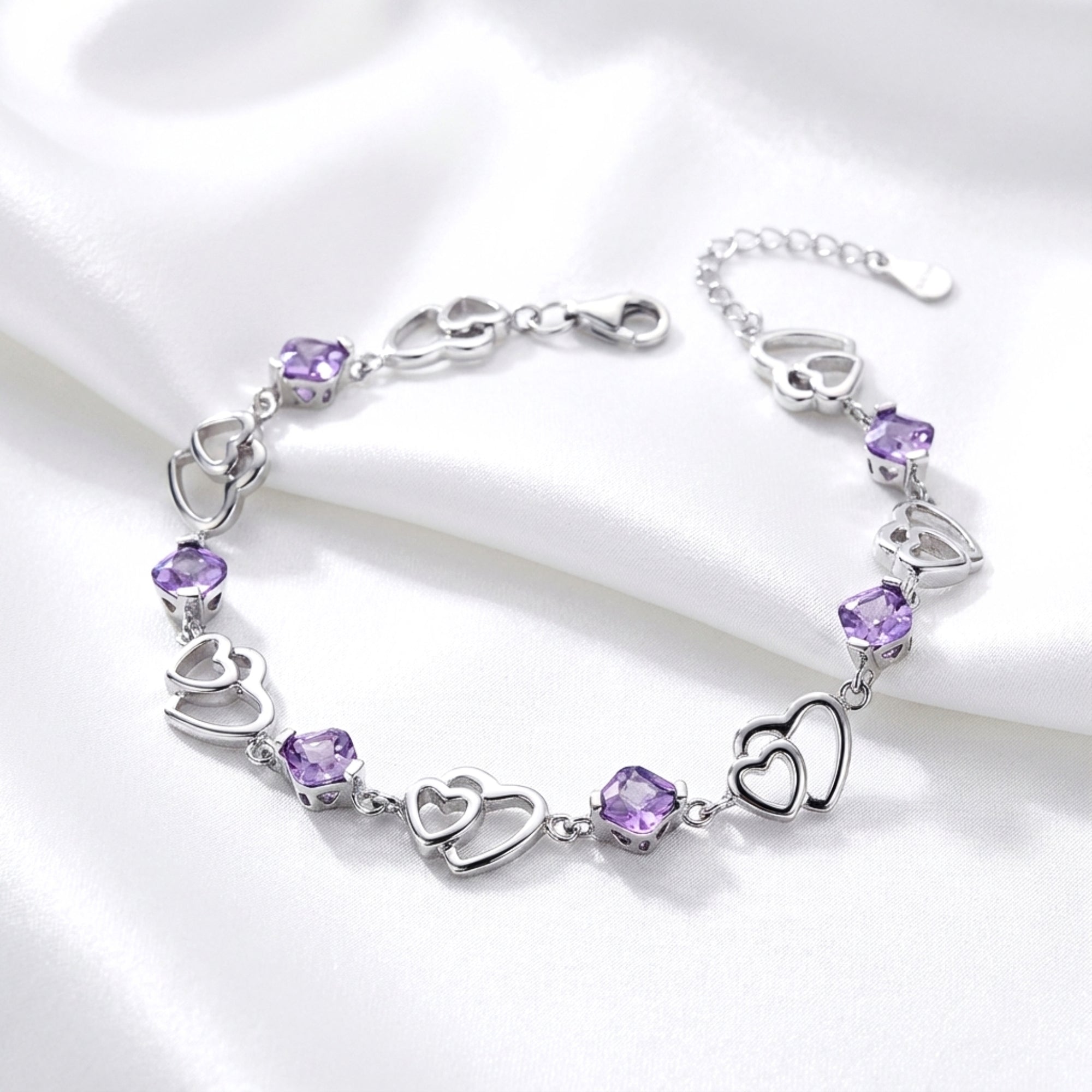 Sterling silver heart link bracelet with purple simulated amethyst stones on white silk.