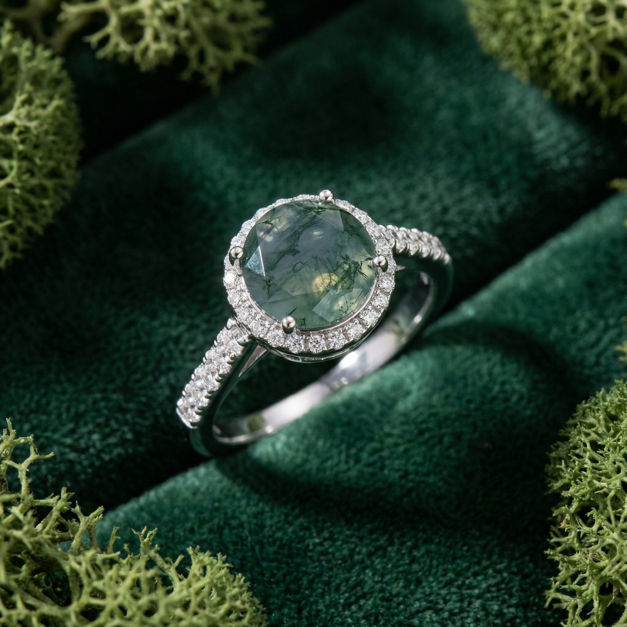 Oval moss agate ring in S925 sterling silver with a diamond halo and accents, shown close-up on green velvet.