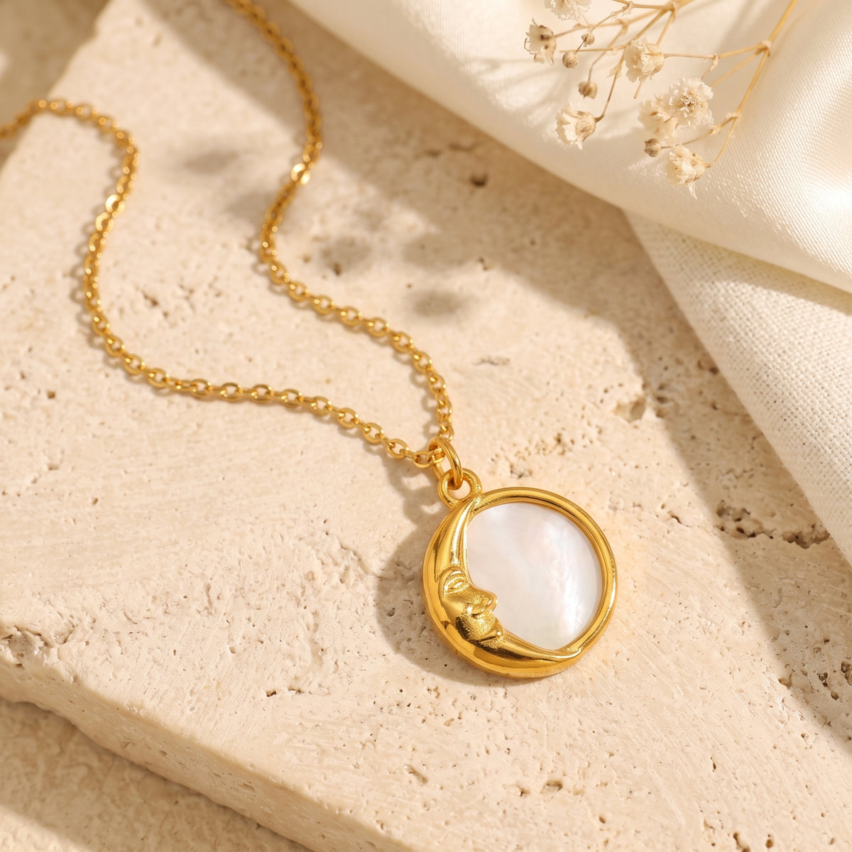 Gold-tone crescent moon pendant with pearlescent inlay on a chain, resting flat on textured stone.