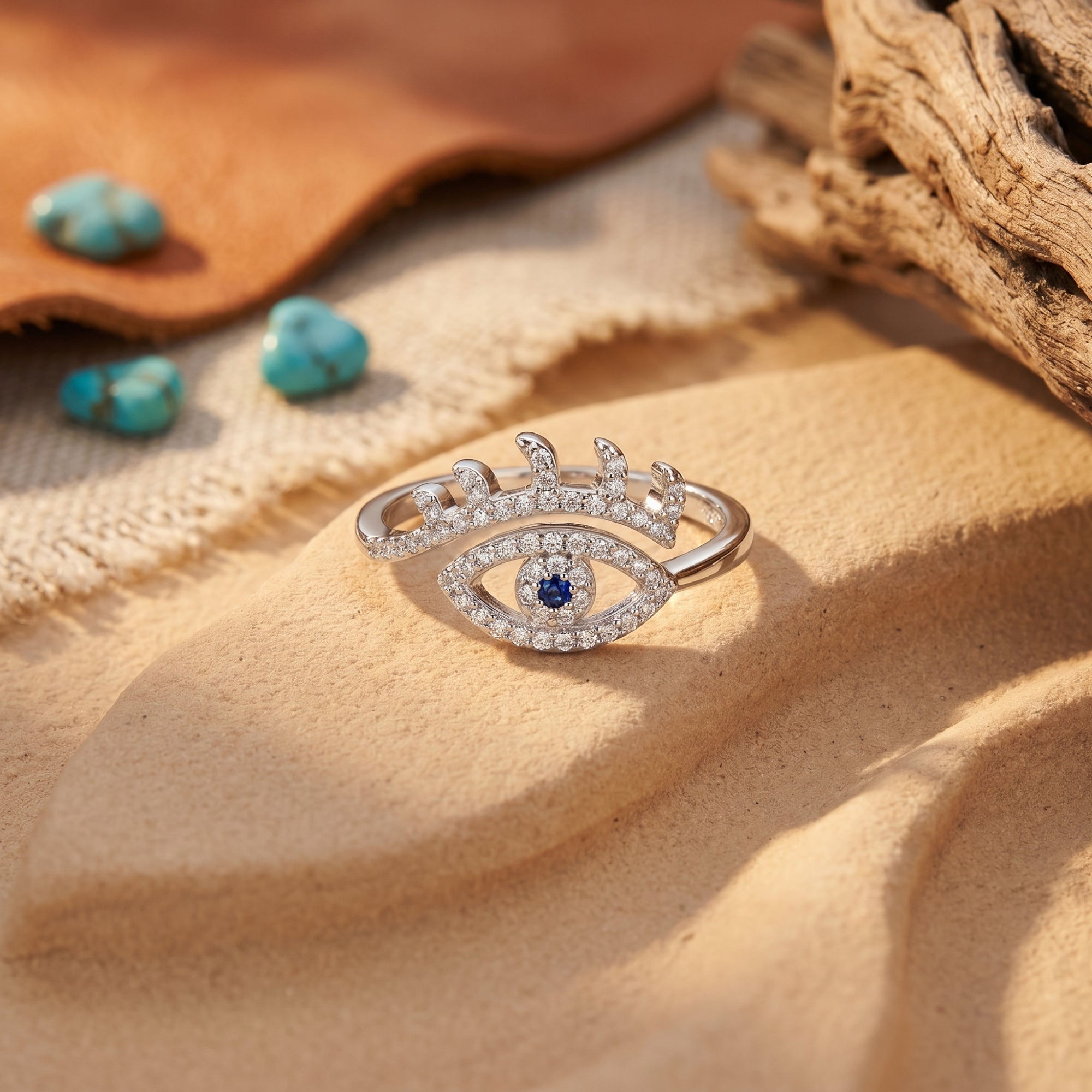 Sterling silver eye-shaped ring with a blue center stone on sand with turquoise stones in the background.