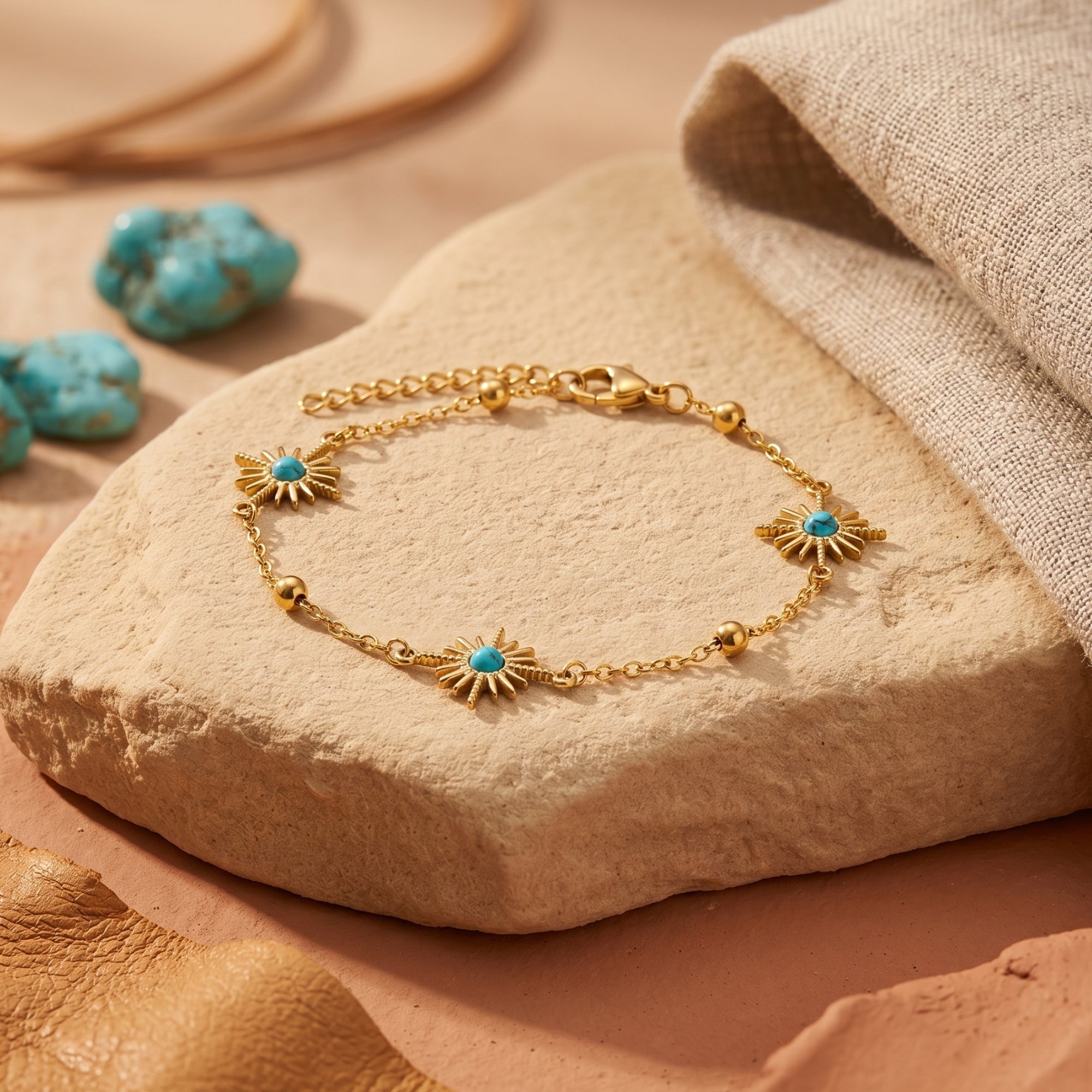 18K gold finish stainless steel chain bracelet with turquoise sunburst charms on a desert stone background.