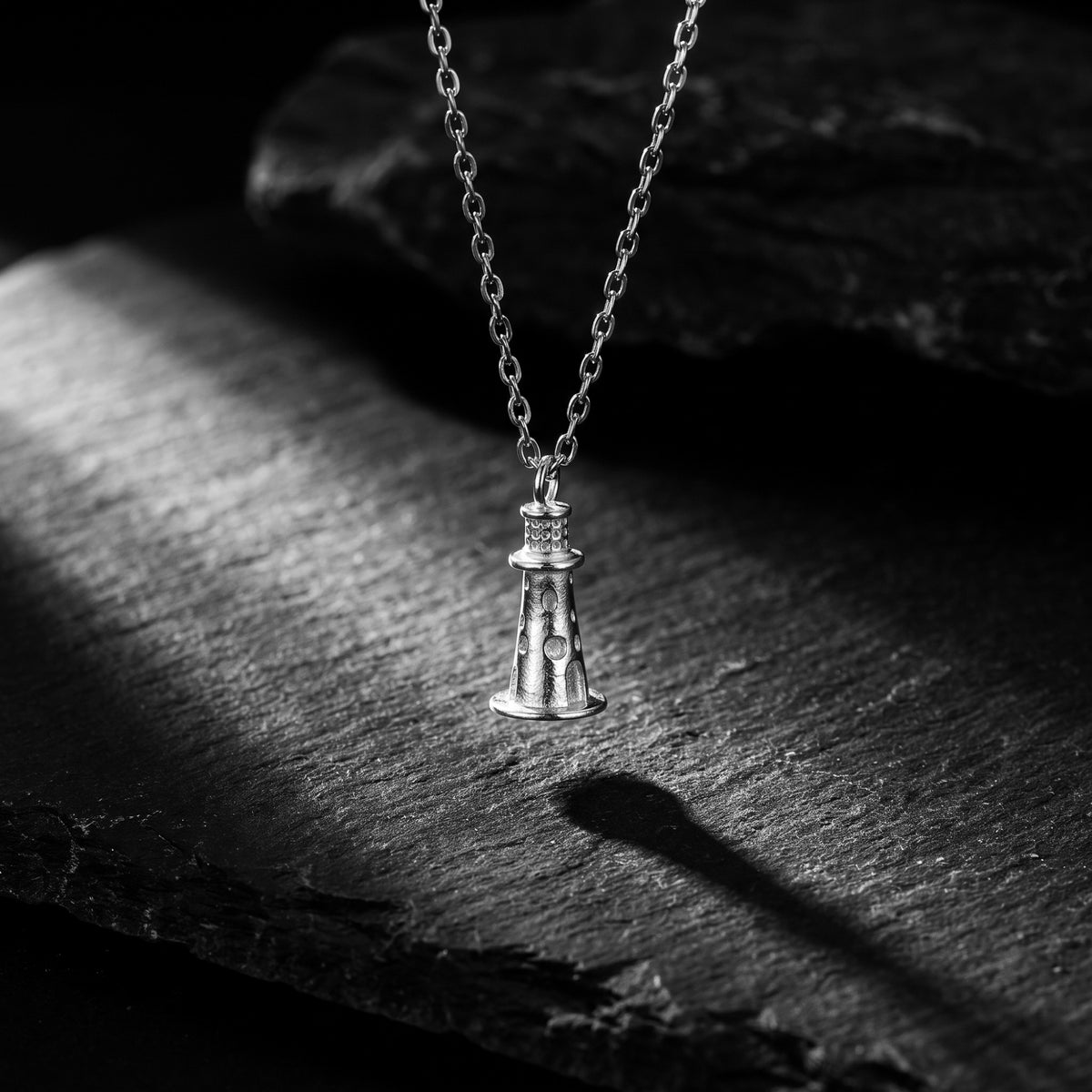 Silver lighthouse pendant necklace hanging vertically over a dark slate surface.