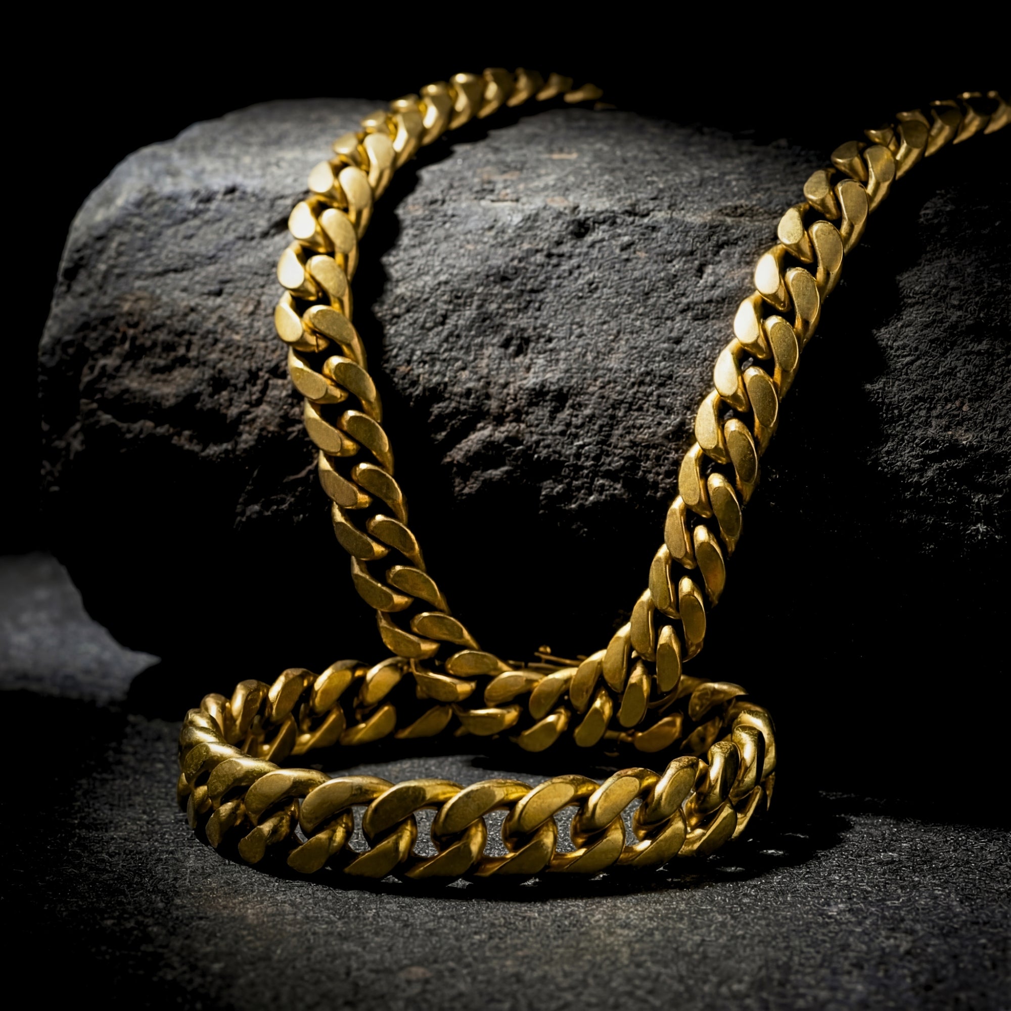 Gold-tone stainless steel Cuban link chain and bracelet set displayed on a dark textured rock.