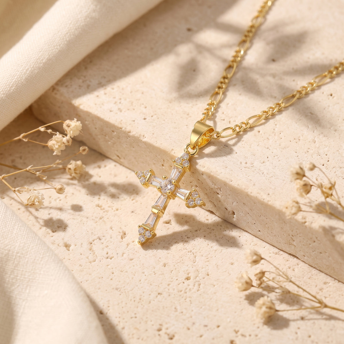 Close-up of a gold-tone cross pendant with clear baguette and round stones on a textured stone surface.
