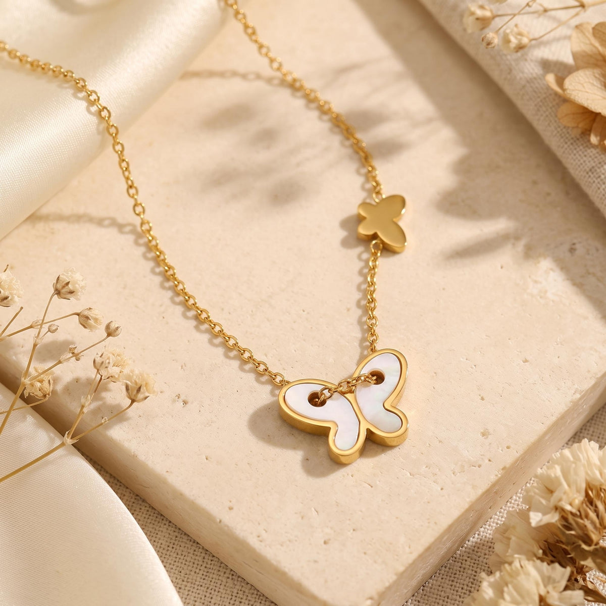 Gold-tone chain necklace with mother-of-pearl butterfly pendant and small gold-tone butterfly charm on a stone slab