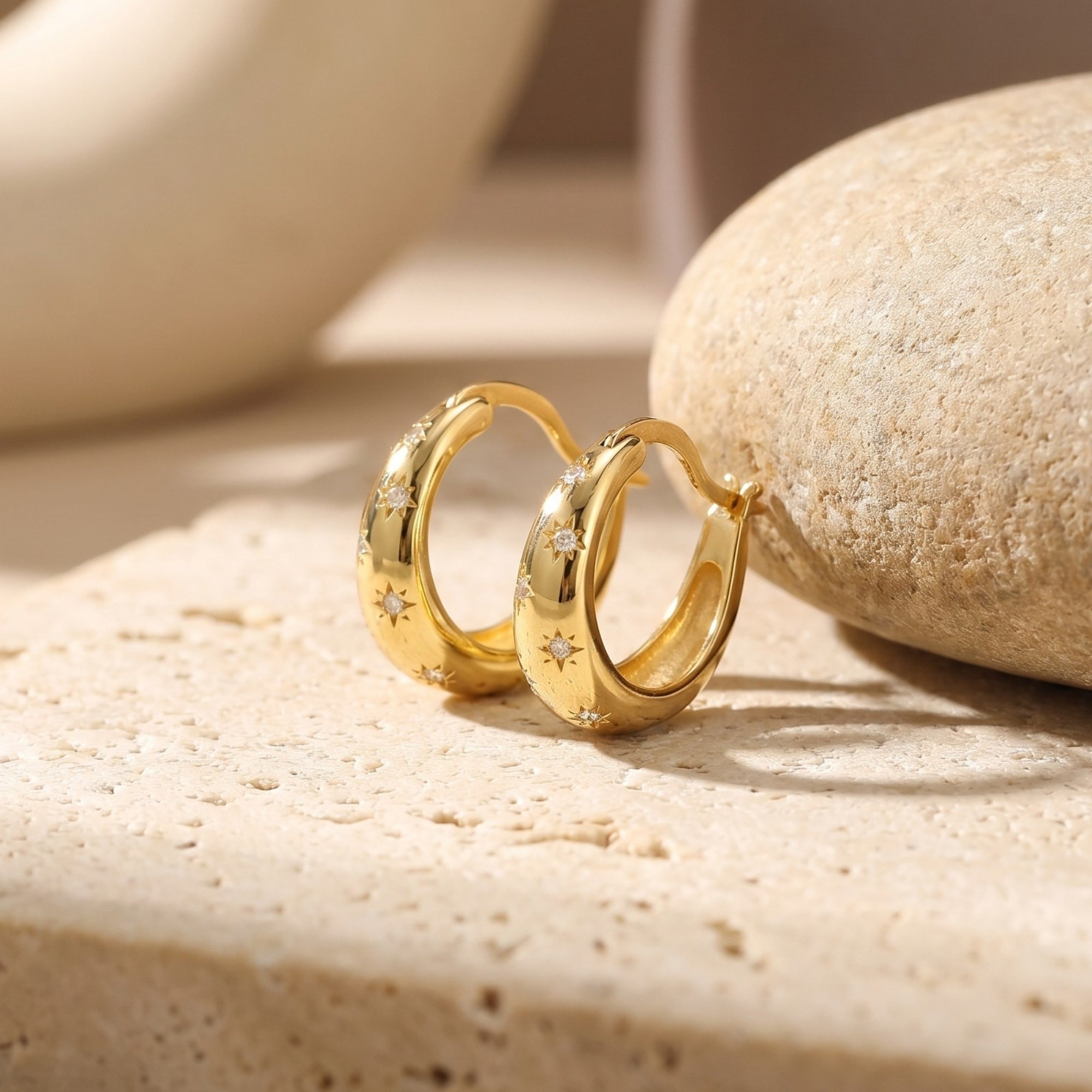 Gold starburst huggie hoop earrings with simulated diamond accents on a textured stone surface.