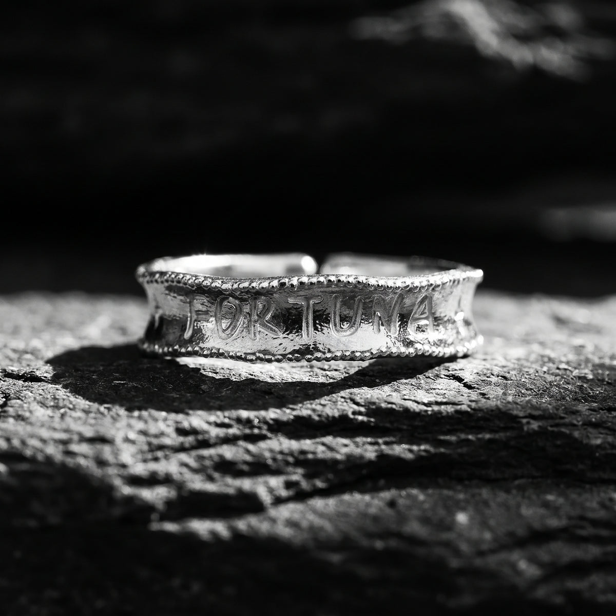 Silver Fortuna ring with milgrain borders resting on dark rock, centered on the front FORTUNA engraving.