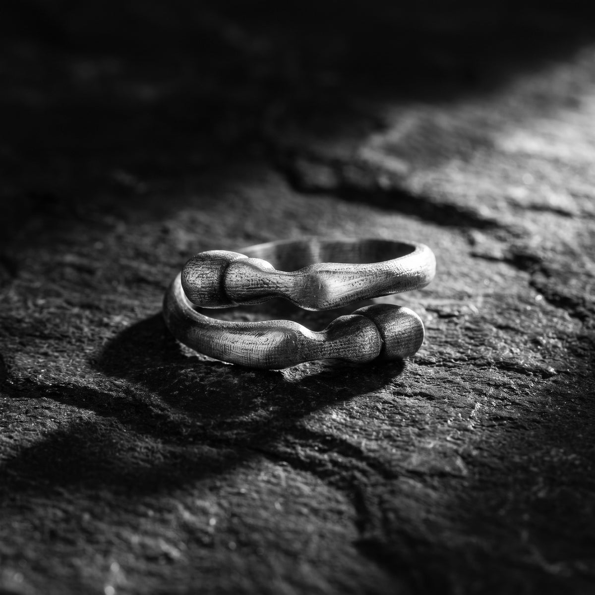 Close-up of a textured 999 fine silver open-band ring resting on a dark, rough rock surface.