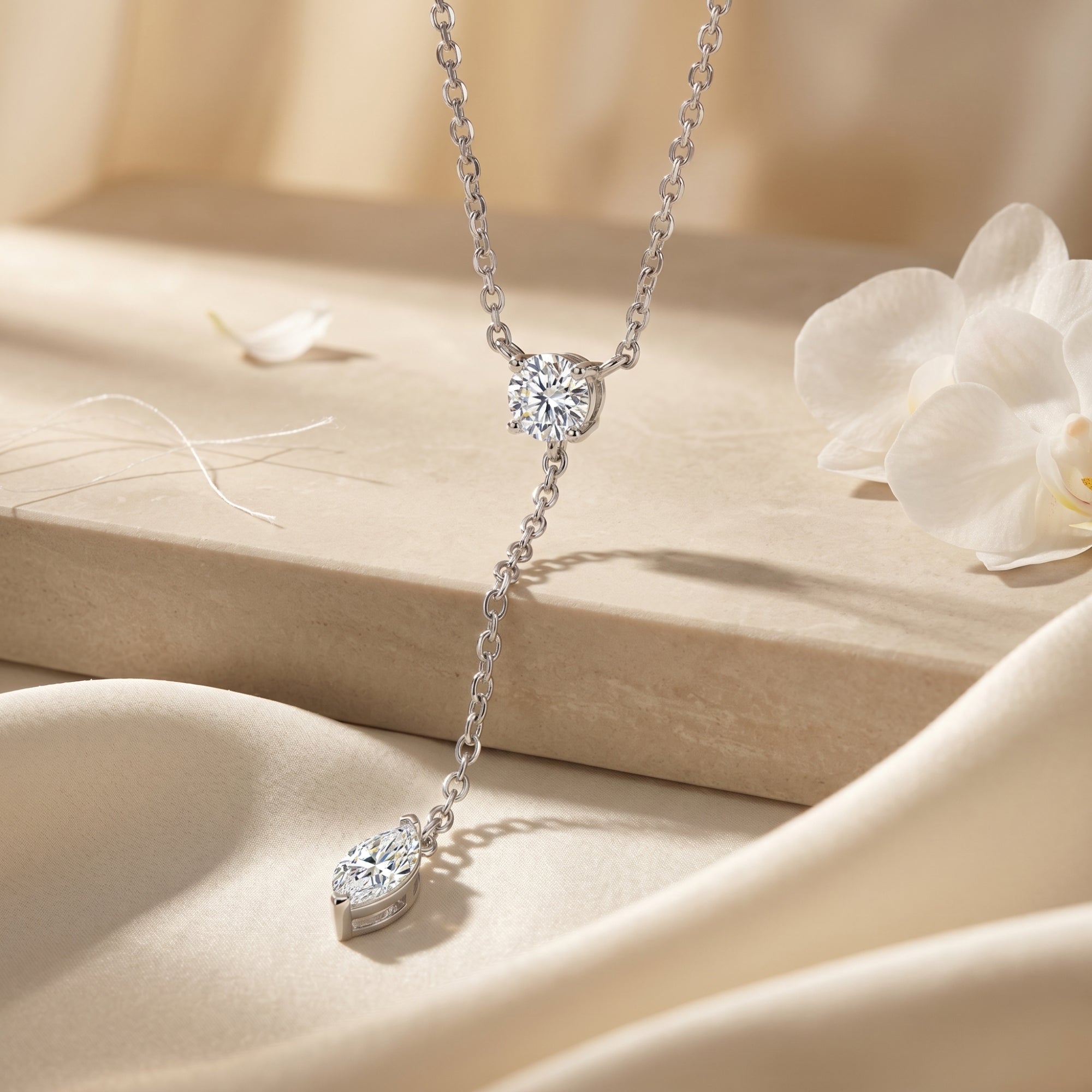 Silver lariat necklace with round and marquise-cut moissanite stones on a stone and silk background.