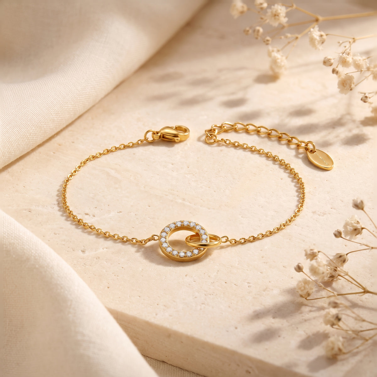 Gold-tone chain bracelet laid flat on a stone surface, with interlocking polished and cubic zirconia-set circles.