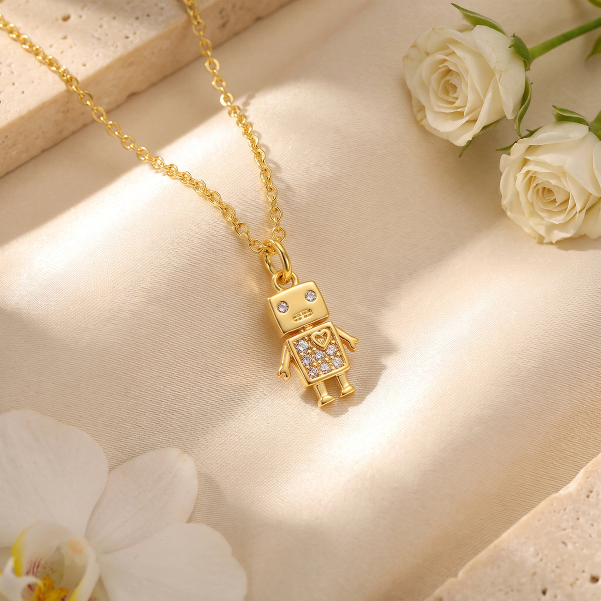 Gold-tone robot pendant necklace with sparkling crystal accents on beige fabric with white flowers.