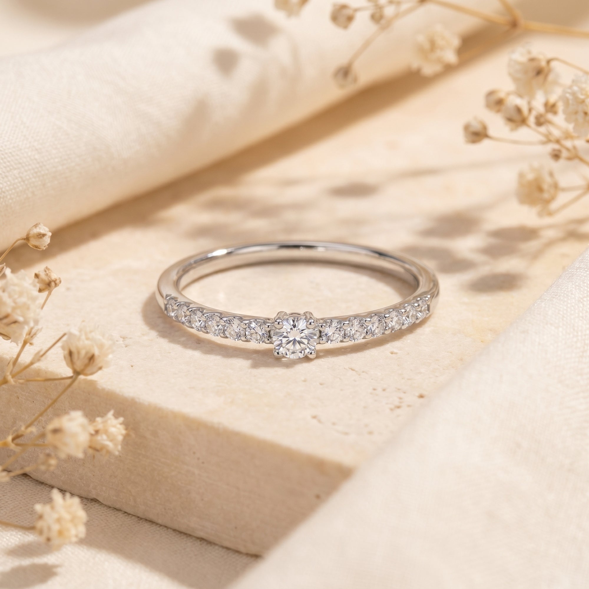 Round moissanite ring in S925 sterling silver with pavé band on a neutral lifestyle background.