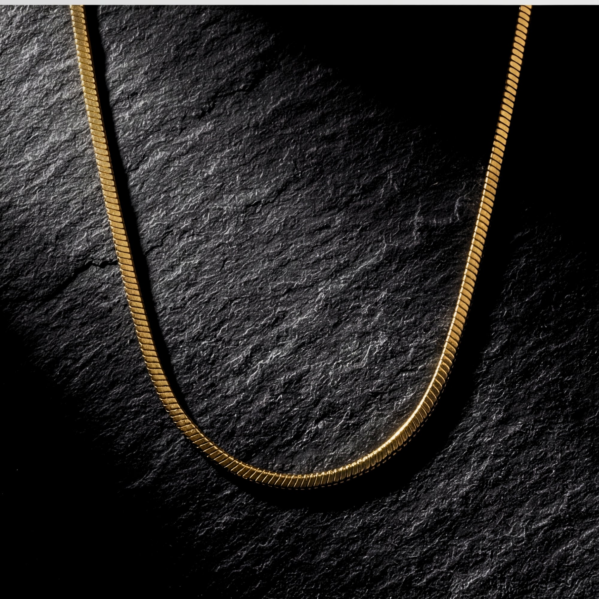 Gold stainless steel Square Dance Chain with square links displayed on a dark textured stone surface.