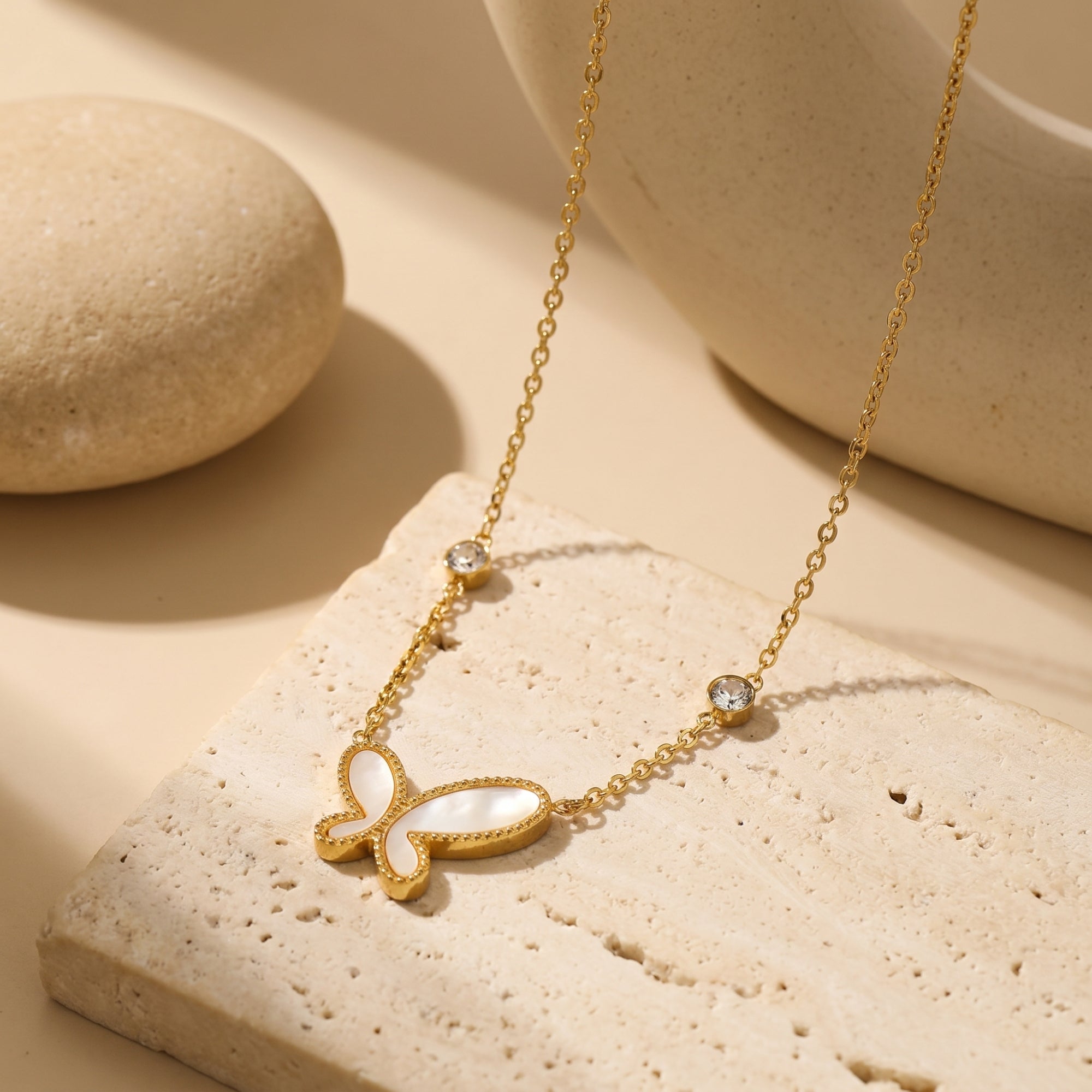 Gold butterfly necklace with mother of pearl inlay on a textured stone block.