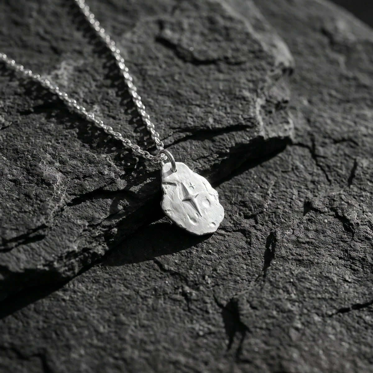 Close-up of the silver starburst pendant resting on textured dark slate.
