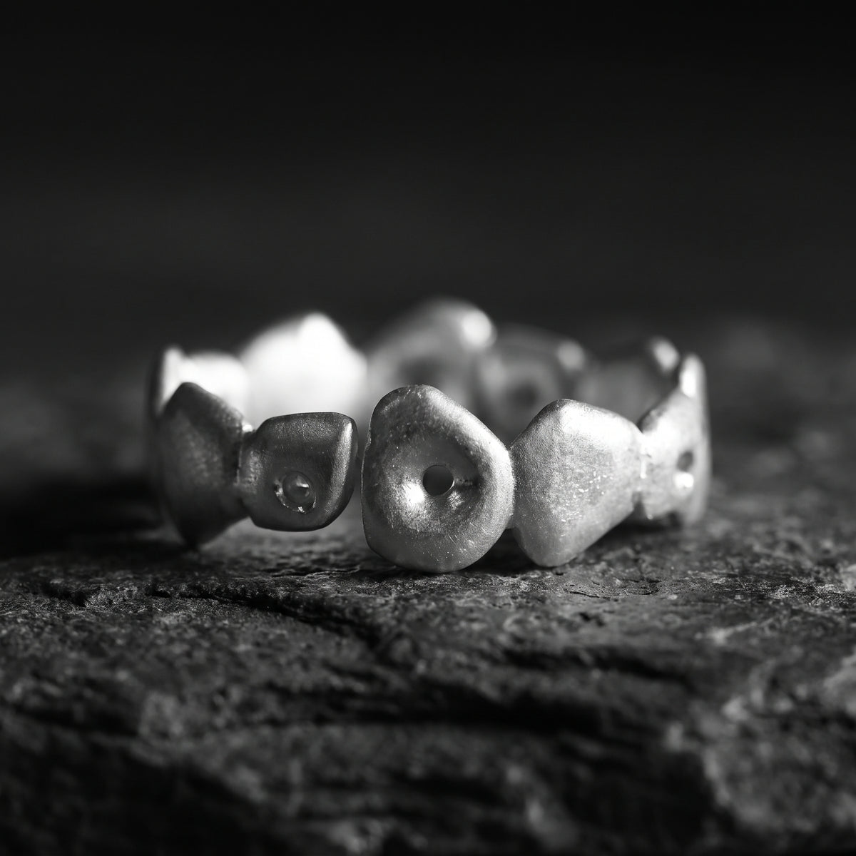 Close-up of the silver pebble open-band ring lying horizontally on a dark, textured rock.