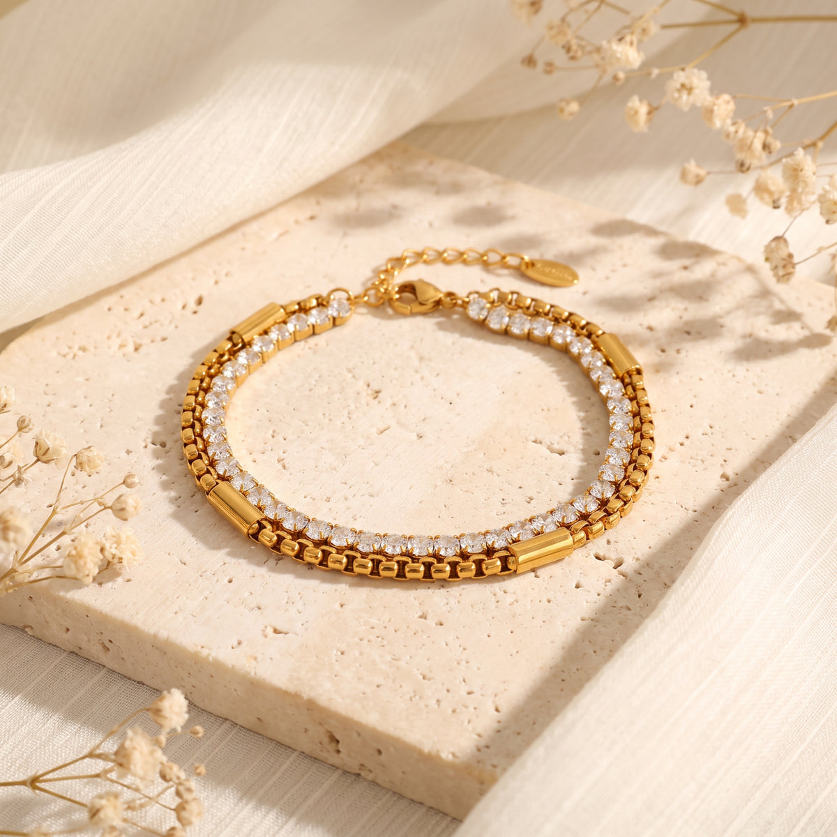 Gold-tone dual-layer bracelet with cubic zirconia and box chain strands displayed on a beige stone tile.