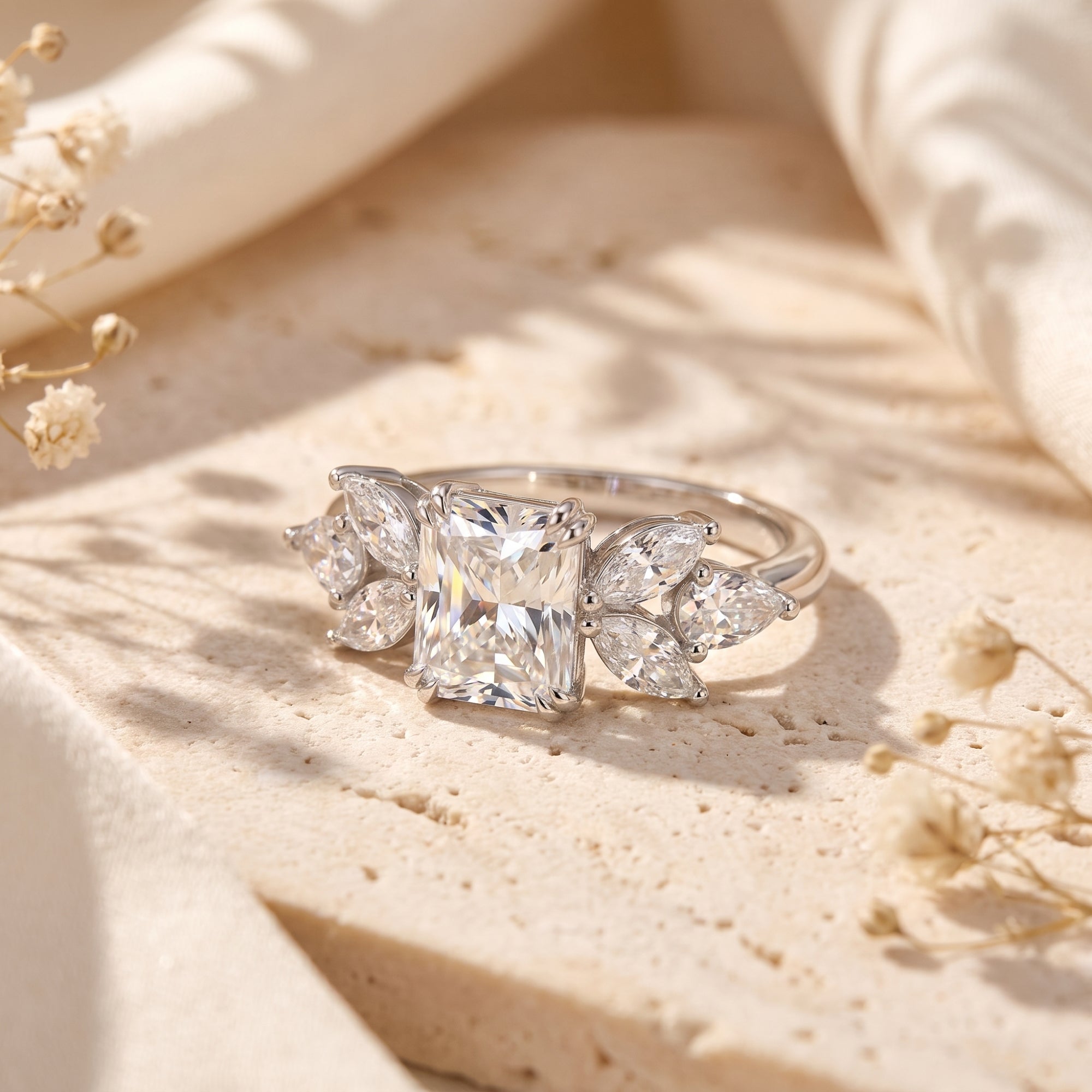 Radiant cut simulated diamond ring in sterling silver on a stone surface with floral accents.