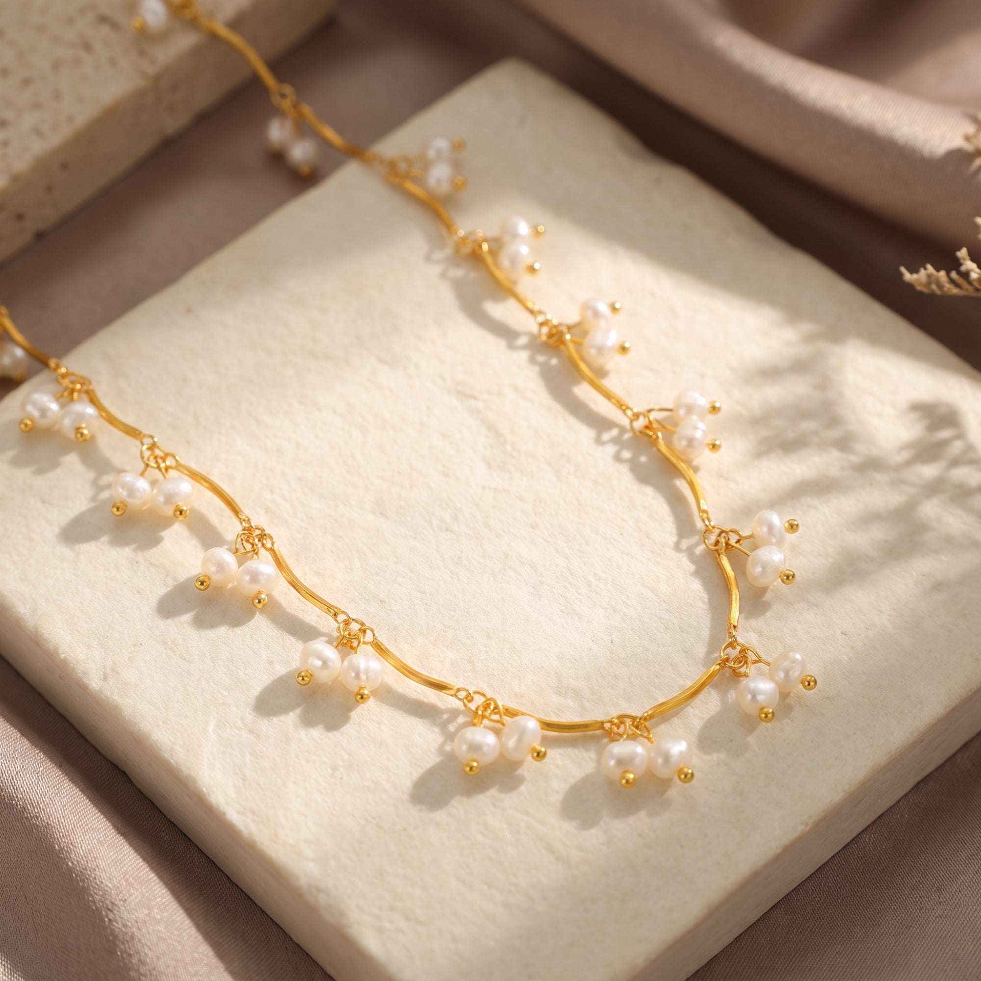 Wavy gold-plated Aurendra necklace with white drop pearls displayed on a textured stone lifestyle backdrop.