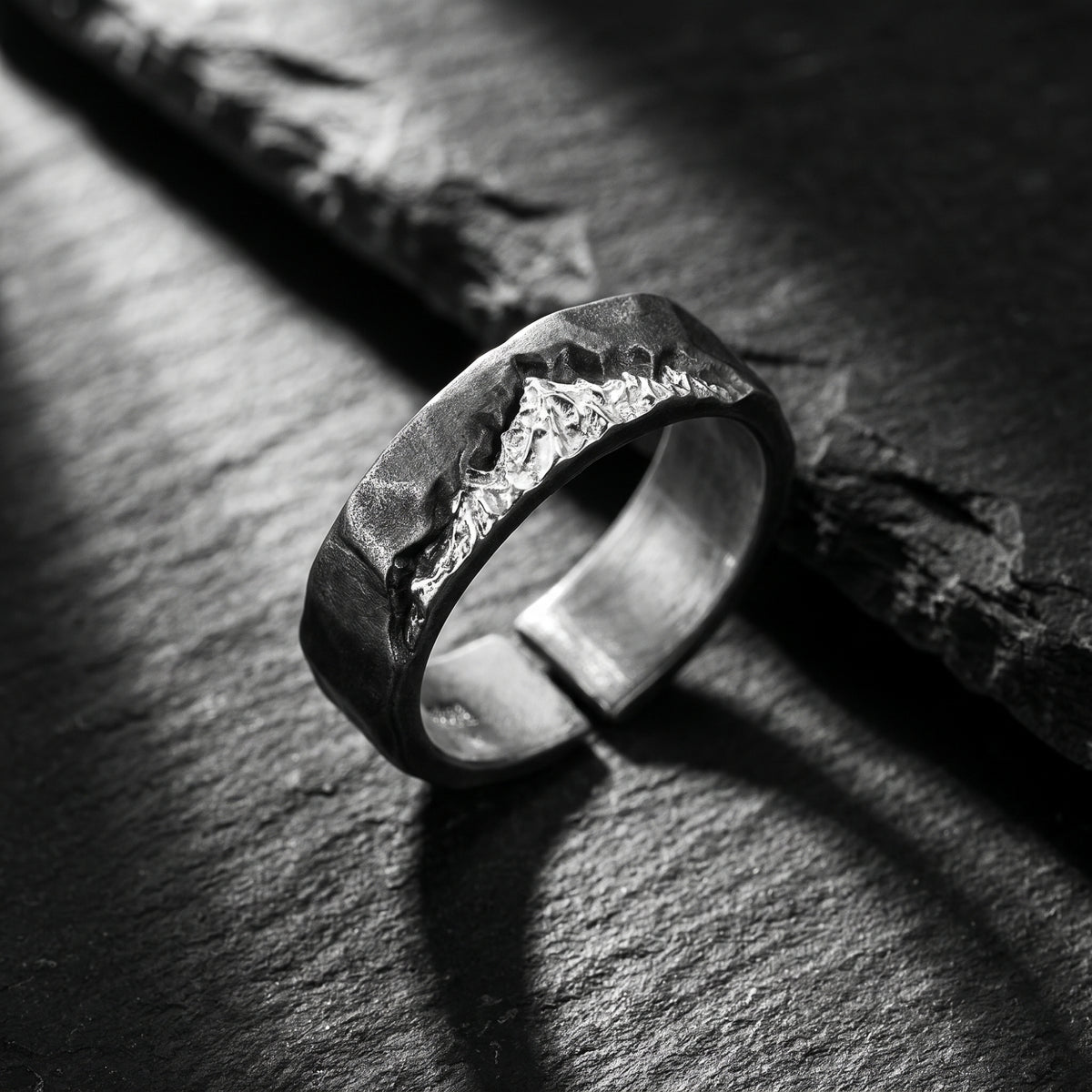 Angled close-up of the silver open ring on dark slate, showing its carved mountain ridge and textured band.