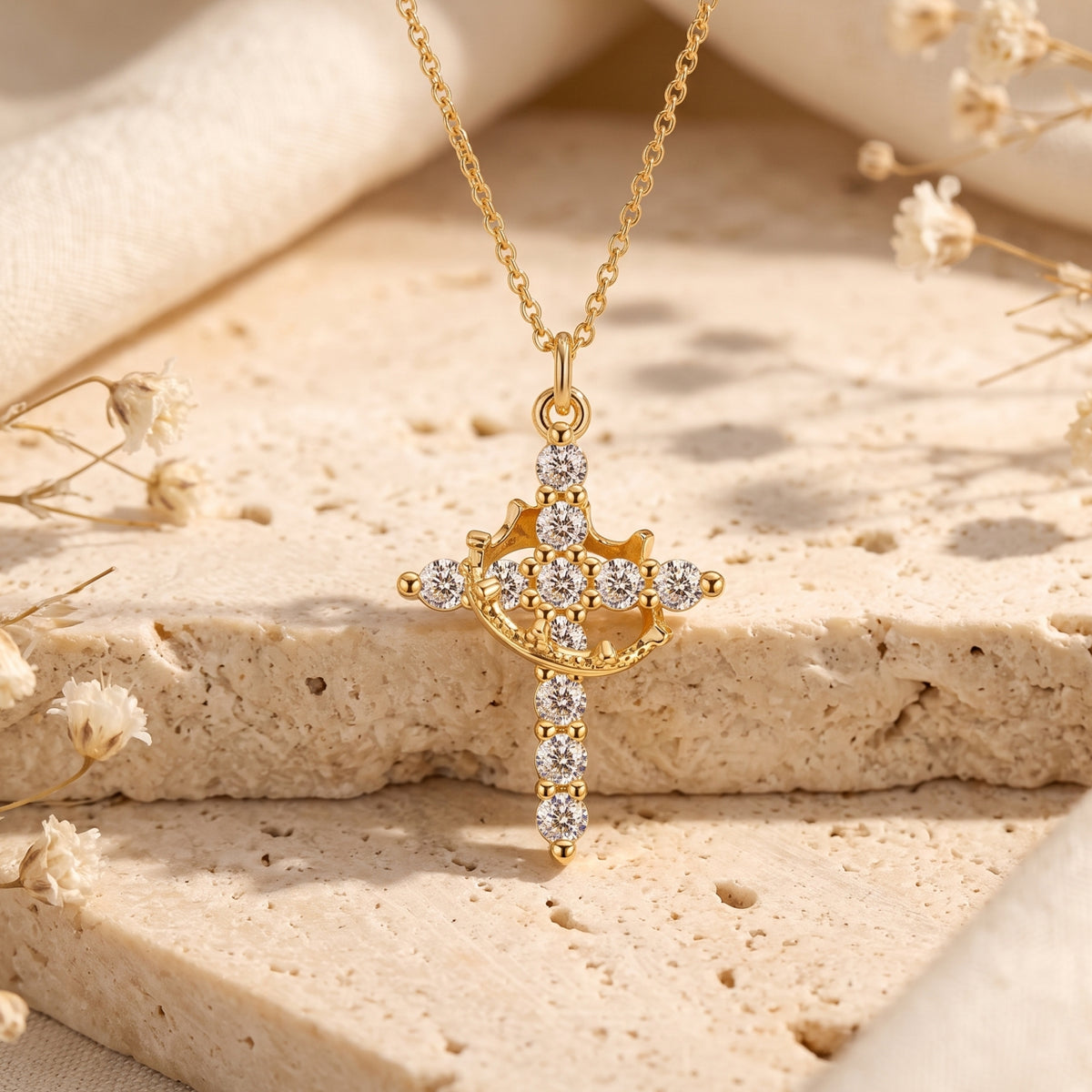 Gold-tone cross pendant with a cubic zirconia crown detail, shown close-up upright on stone.