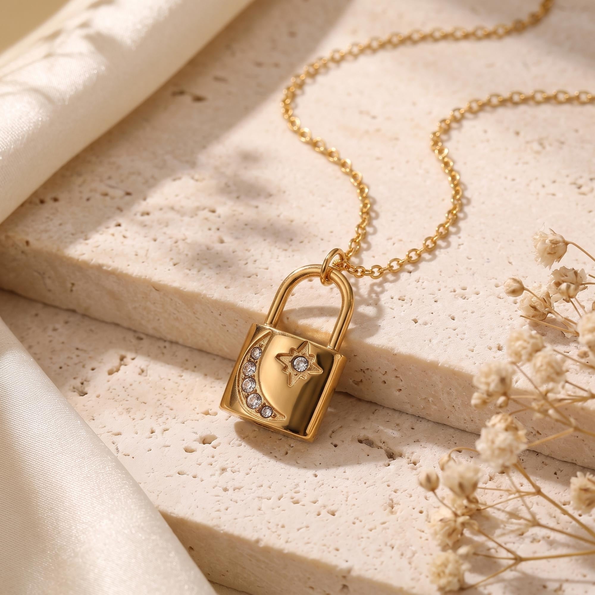 Gold padlock pendant necklace with moon and star simulated diamonds on a stone surface.