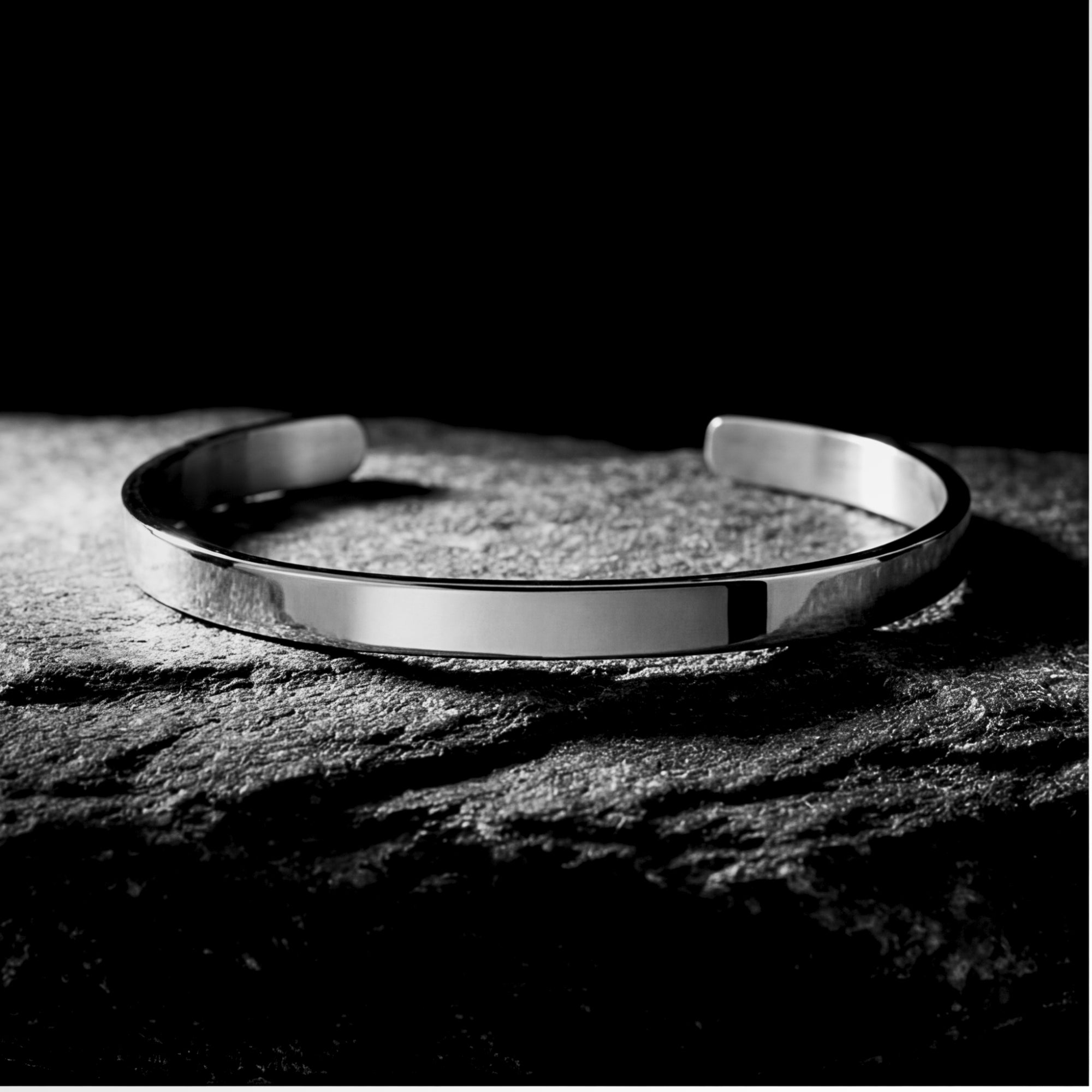 Silver stainless steel cuff bracelet resting on a dark textured rock surface.