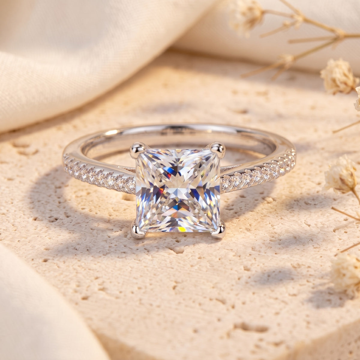 Front view of a silver ring with a large princess-cut center stone and pave accent stones on a stone surface.