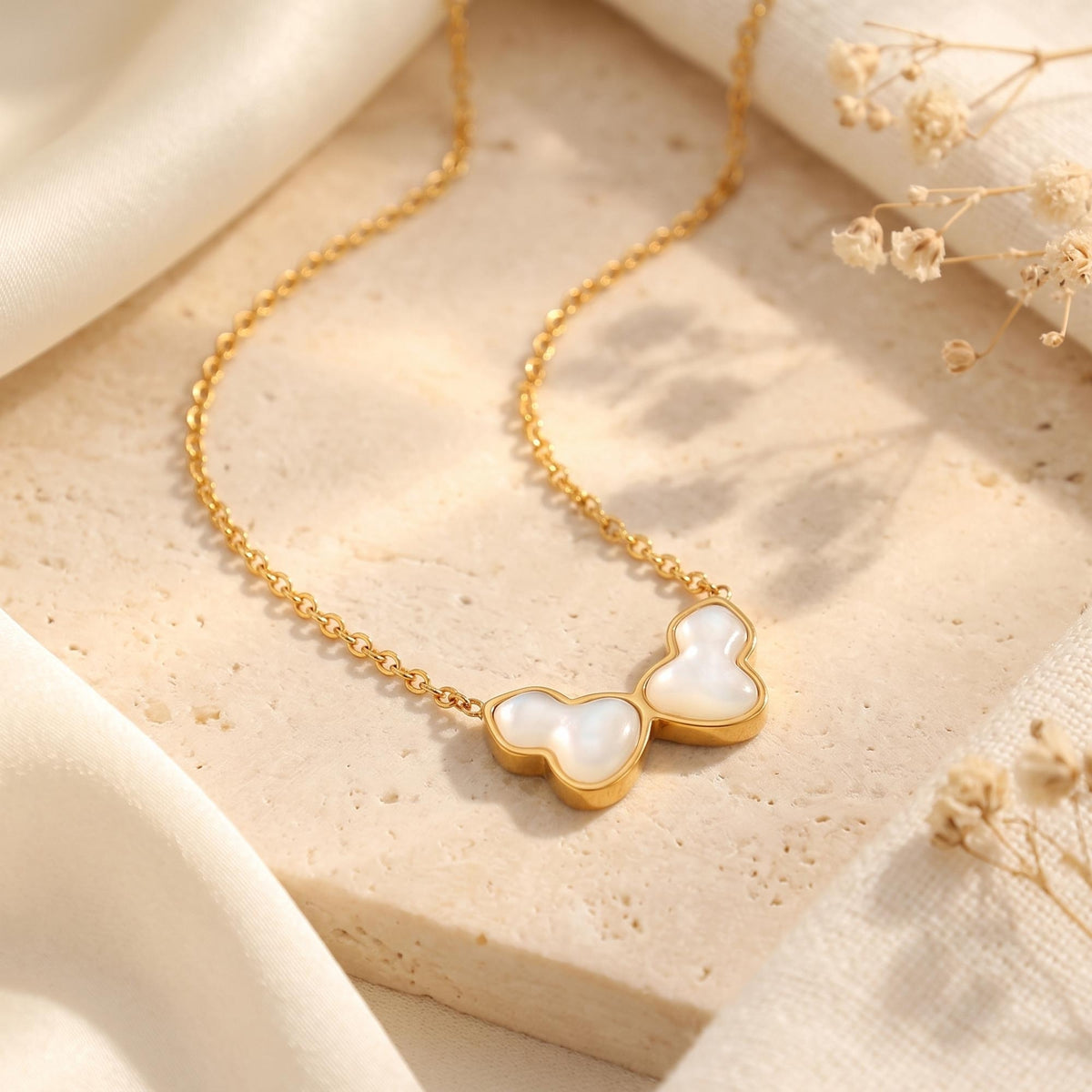 Gold-tone chain necklace with a stylized butterfly pendant and white iridescent inlays on a light stone surface.